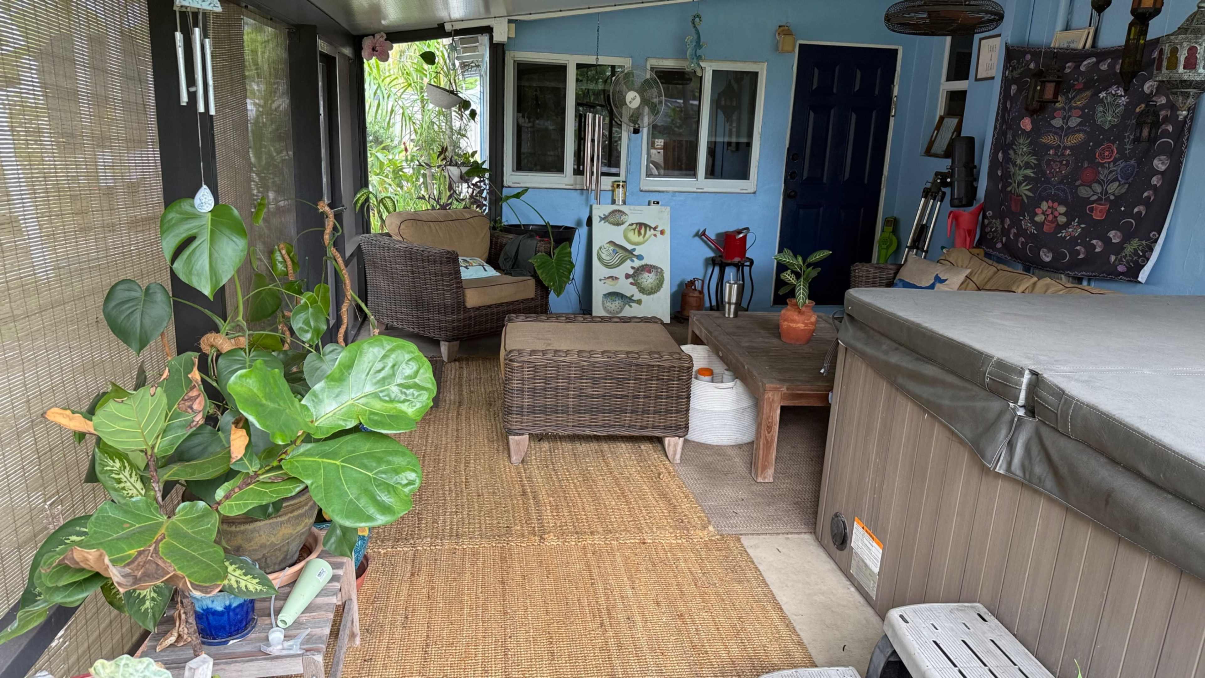 The image shows a covered porch area with wicker furniture, potted plants, a hot tub, and a decorative wall.