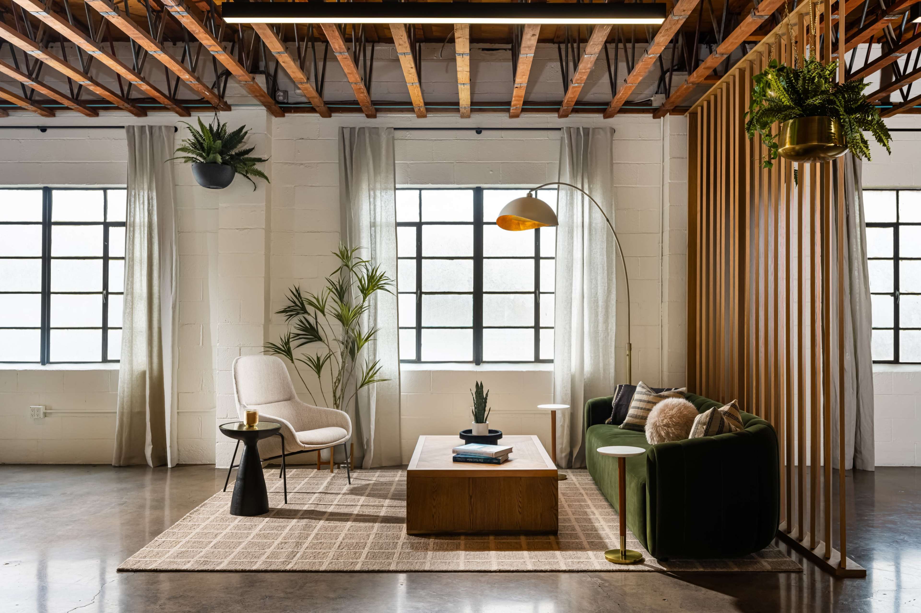 The image depicts a stylish living room featuring a green sofa, a wooden coffee table, an arching floor lamp, and plants, with large windows allowing natural light to fill the space.