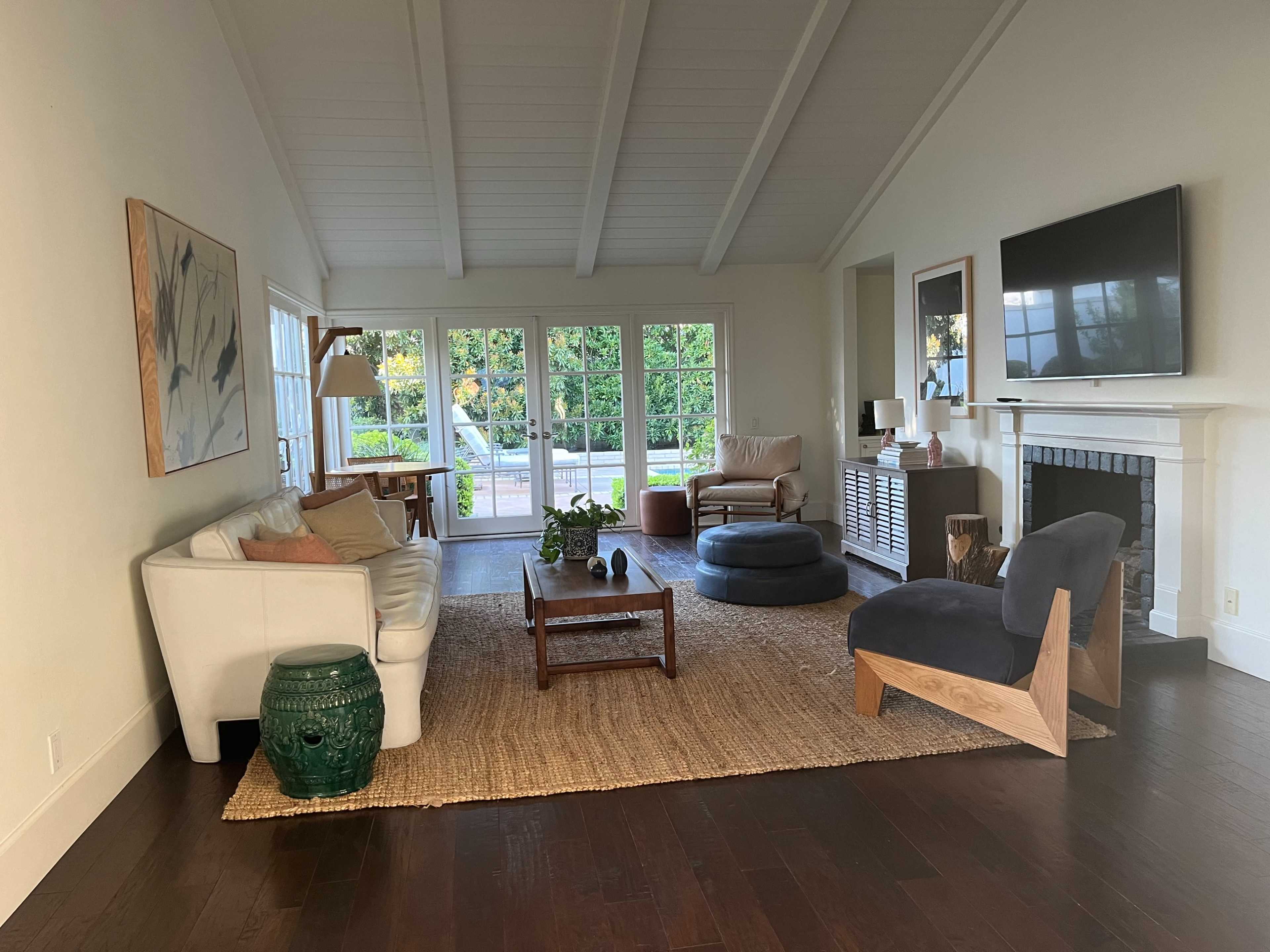 The image shows a spacious living room with a white sofa, a green side table, and a large window letting in natural light.