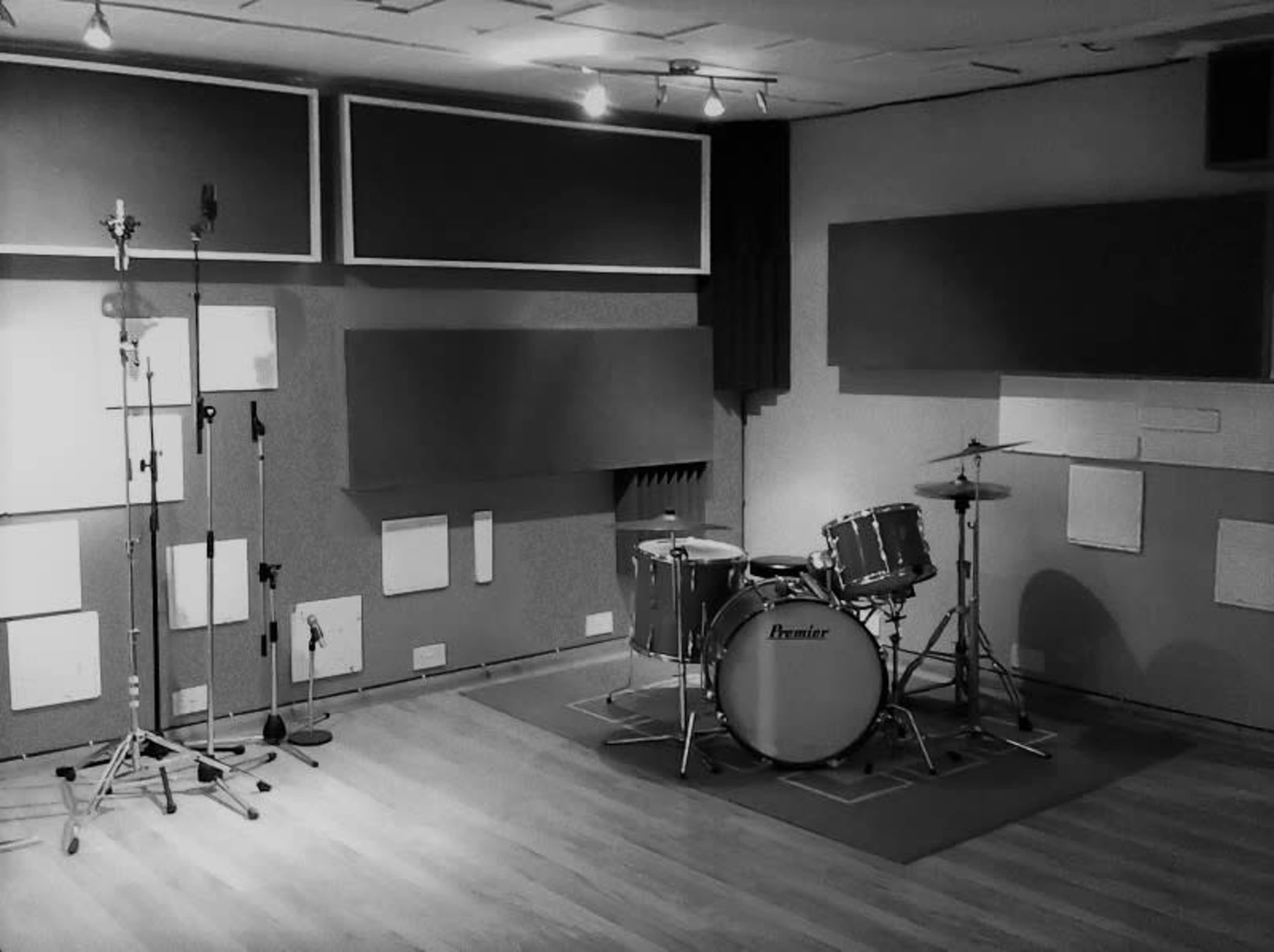 A soundproof recording studio with a drum set and microphone stands positioned against padded walls.