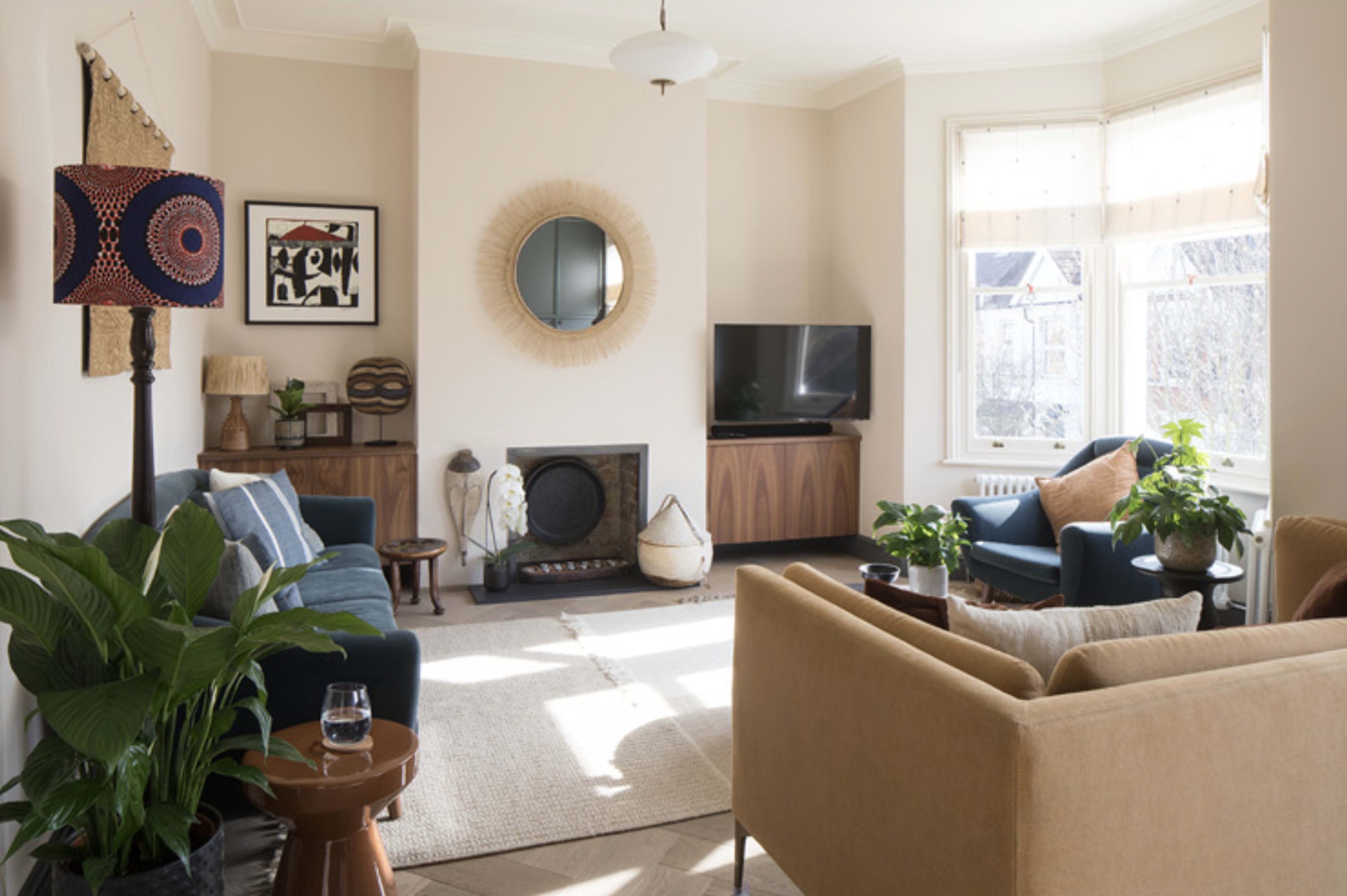The living room features two sofas, a coffee table, a television, and several plants, illuminated by natural light from the large windows.