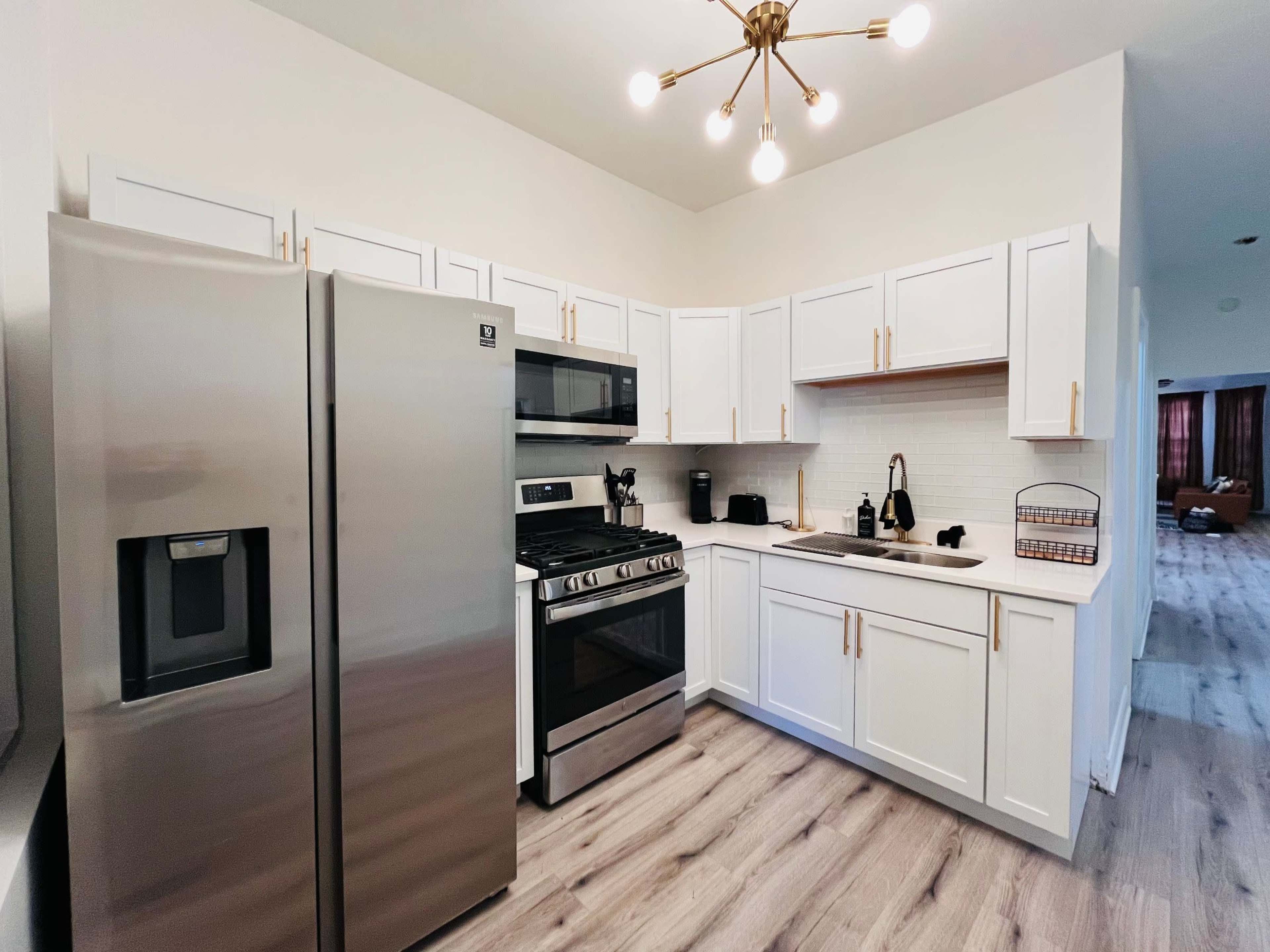 A modern kitchen features stainless steel appliances, white cabinetry, and wooden flooring.