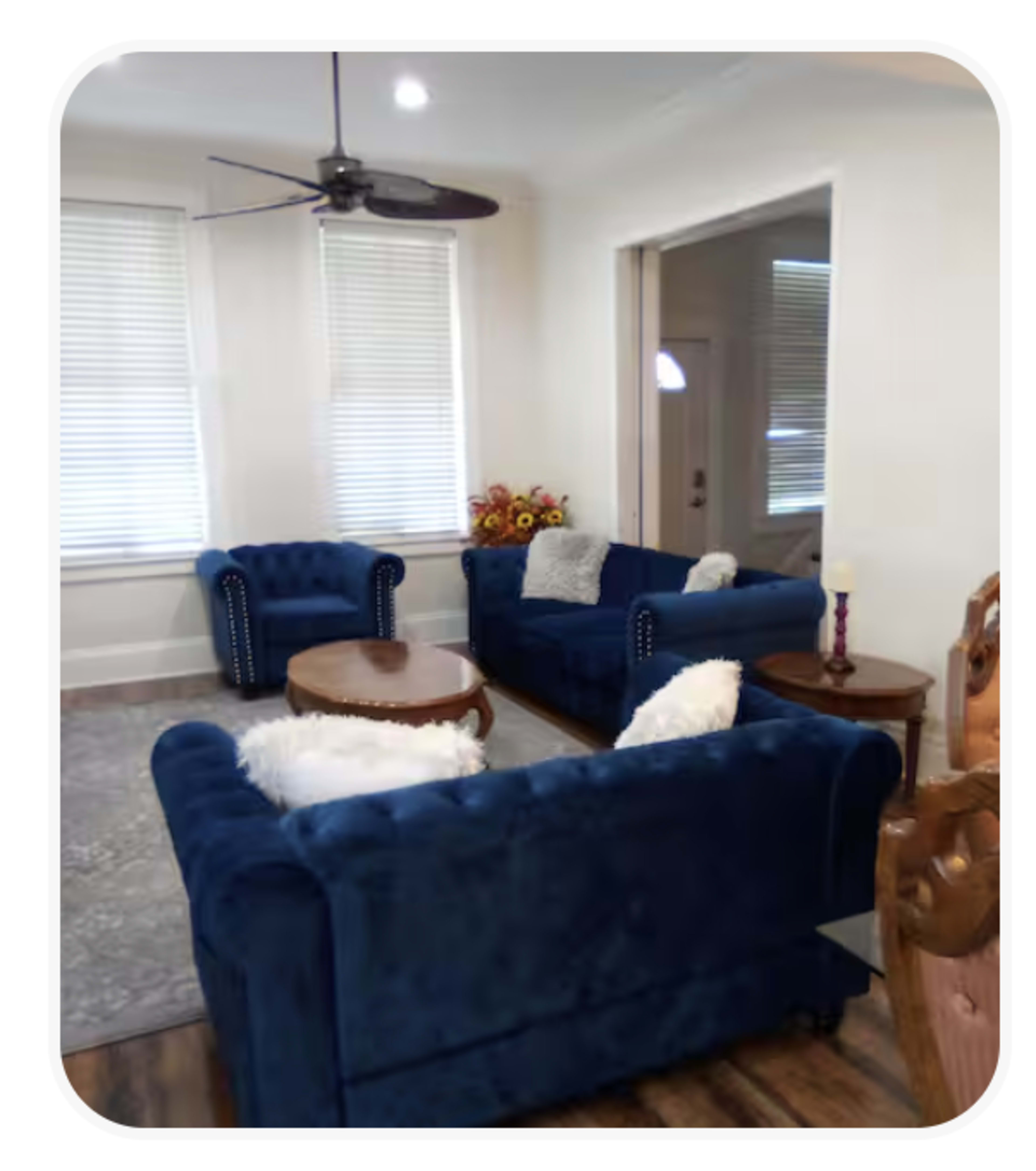 The living room features two blue velvet sofas, a wooden coffee table, and a floral arrangement, all arranged on a light gray rug.
