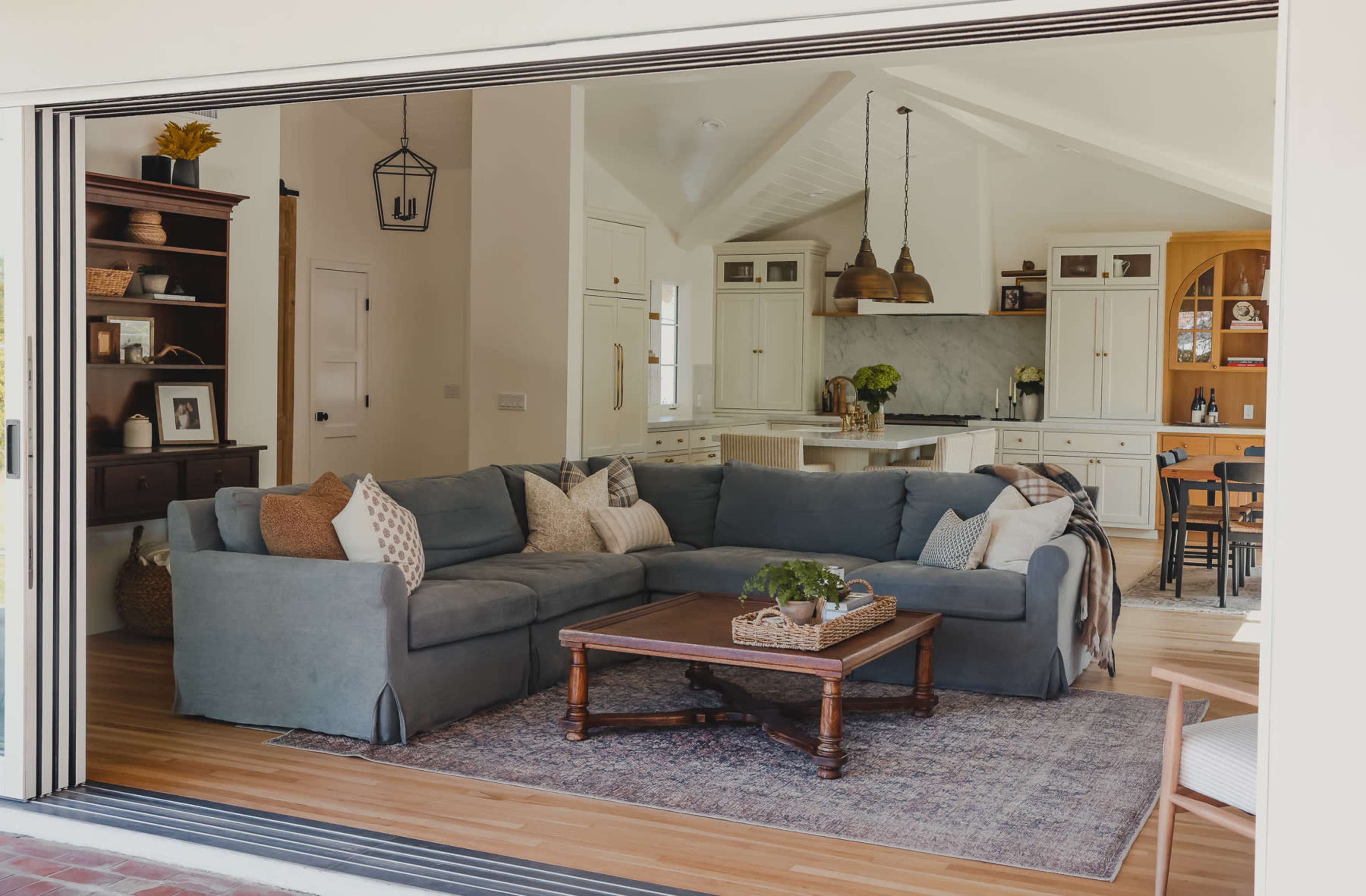 A spacious living room with a blue sectional sofa and a wooden coffee table opens up to a bright kitchen area.