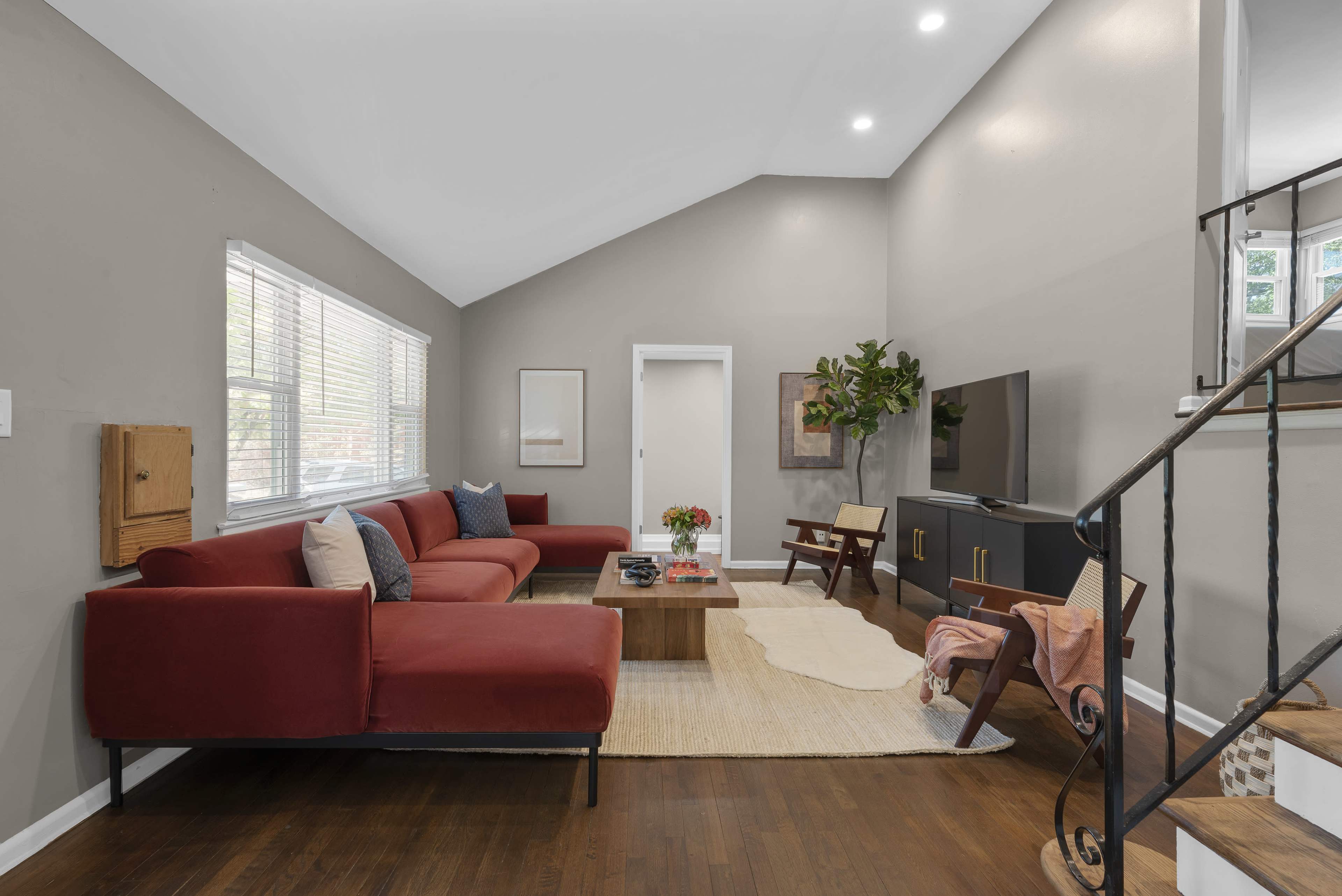 The living room features a red sectional sofa, a wooden coffee table, and a television against a gray wall, with stairs leading to an upper level.