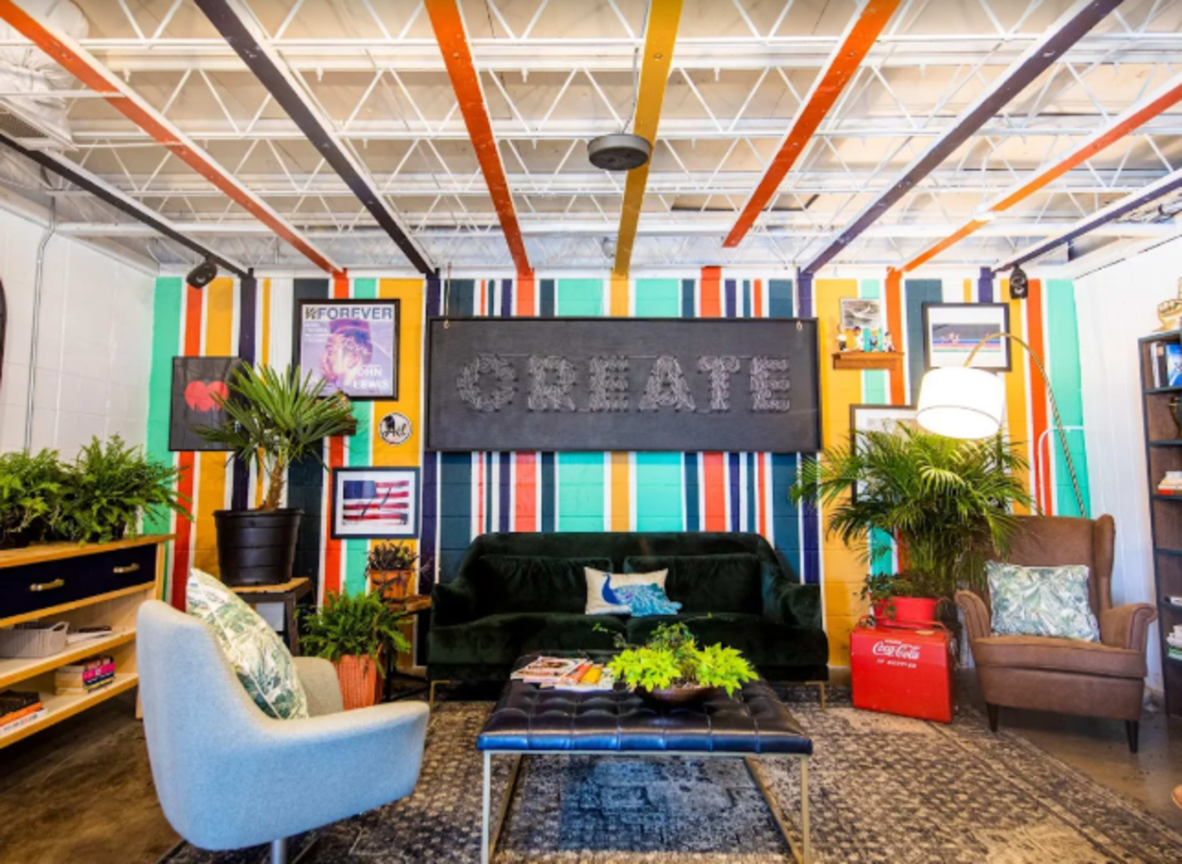 The image depicts a colorful lounge area featuring a green velvet sofa, an armchair, decorative plants, a coffee table, and a large wall sign that says "CREATE."