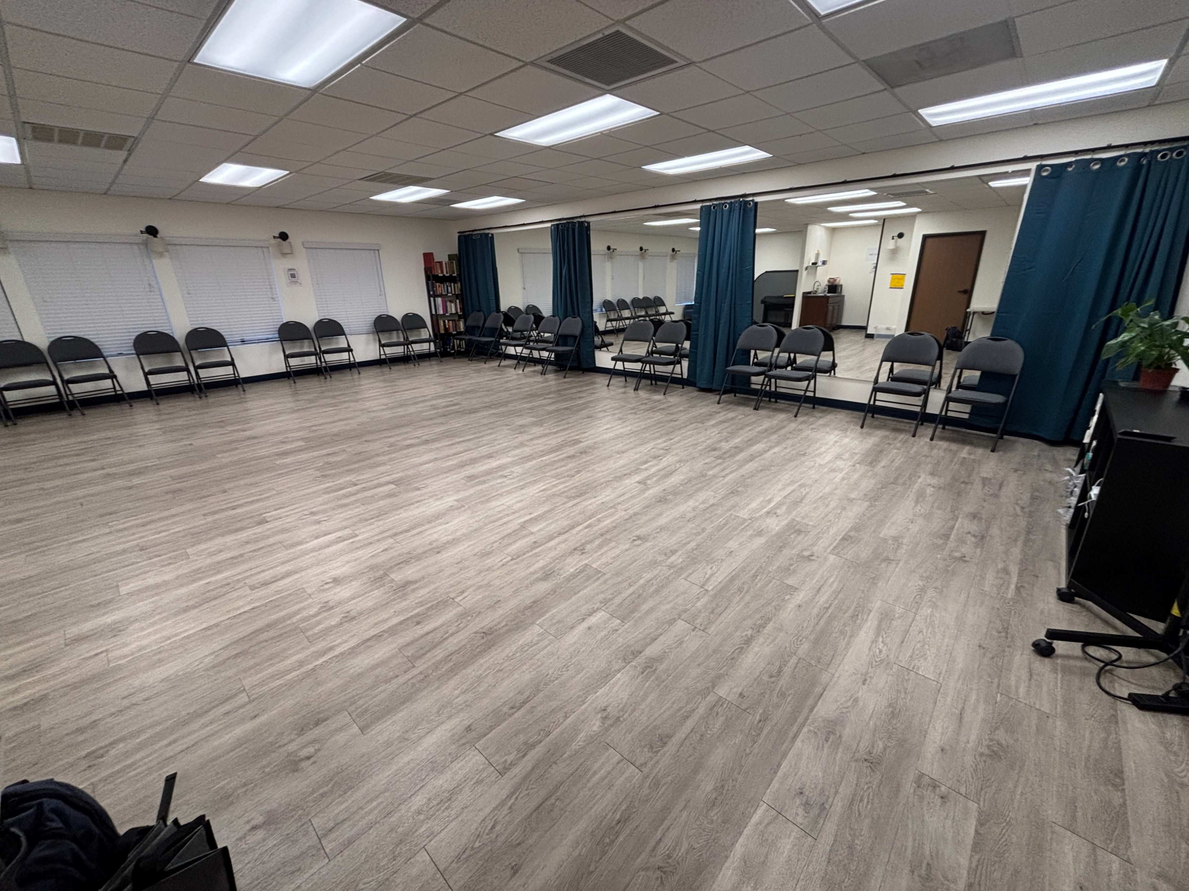 The image shows an empty meeting room with rows of chairs, mirrors on one wall, and wooden flooring.
