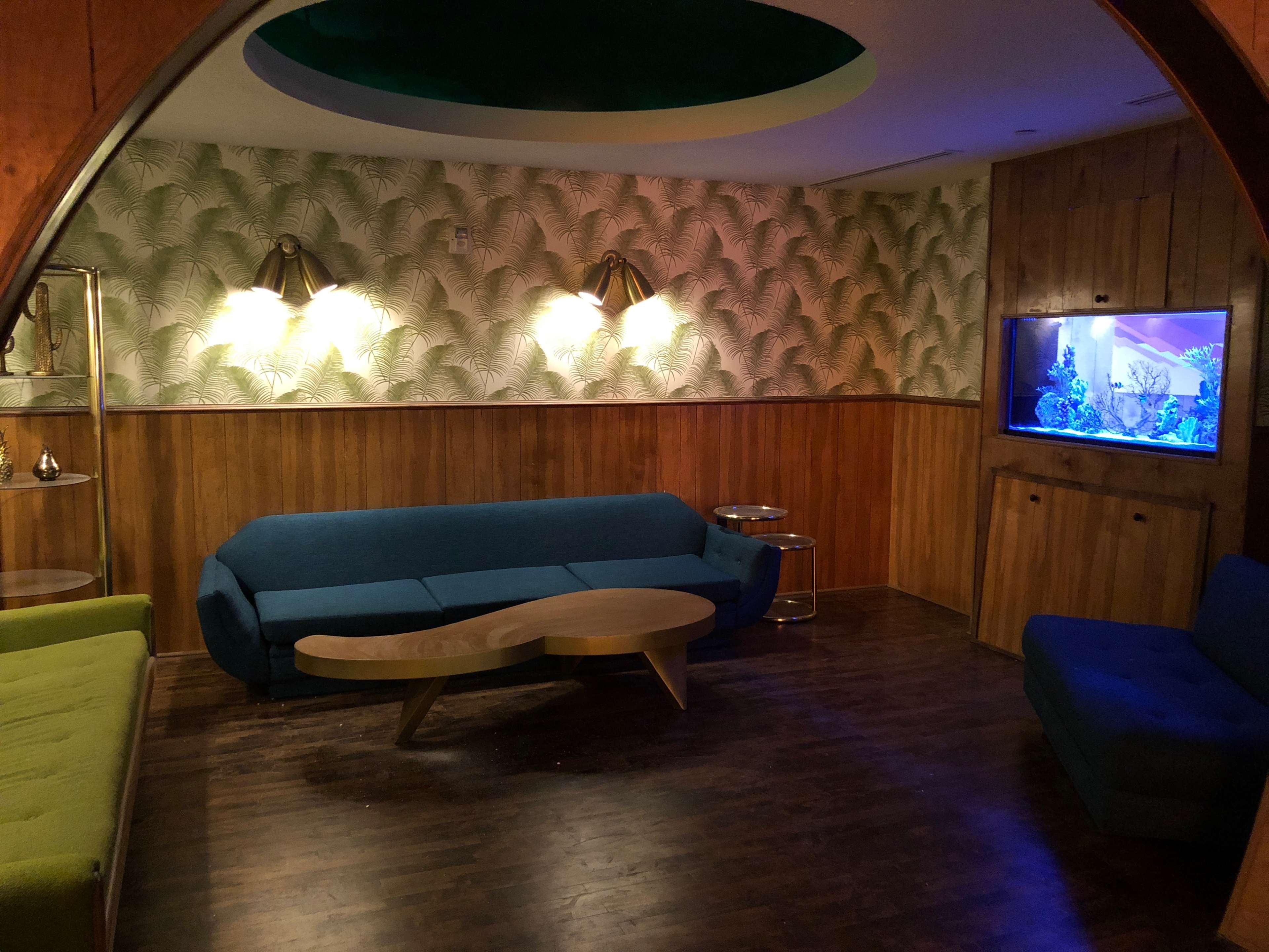 A decorated lounge area with two sofas, a coffee table, and an aquarium against a wall featuring plant-patterned wallpaper.