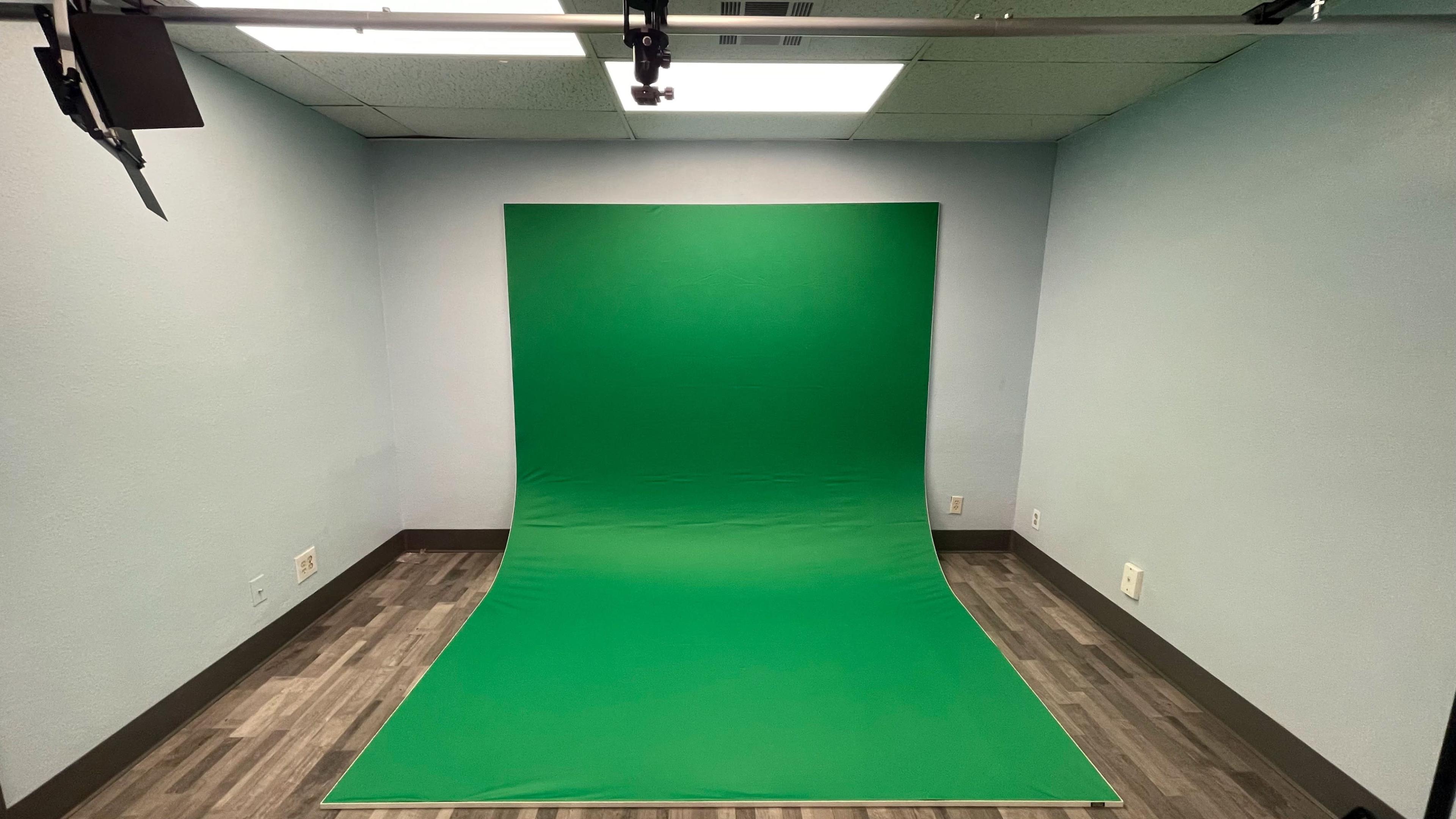 A room with a green screen setup against a light blue wall and a wooden floor.