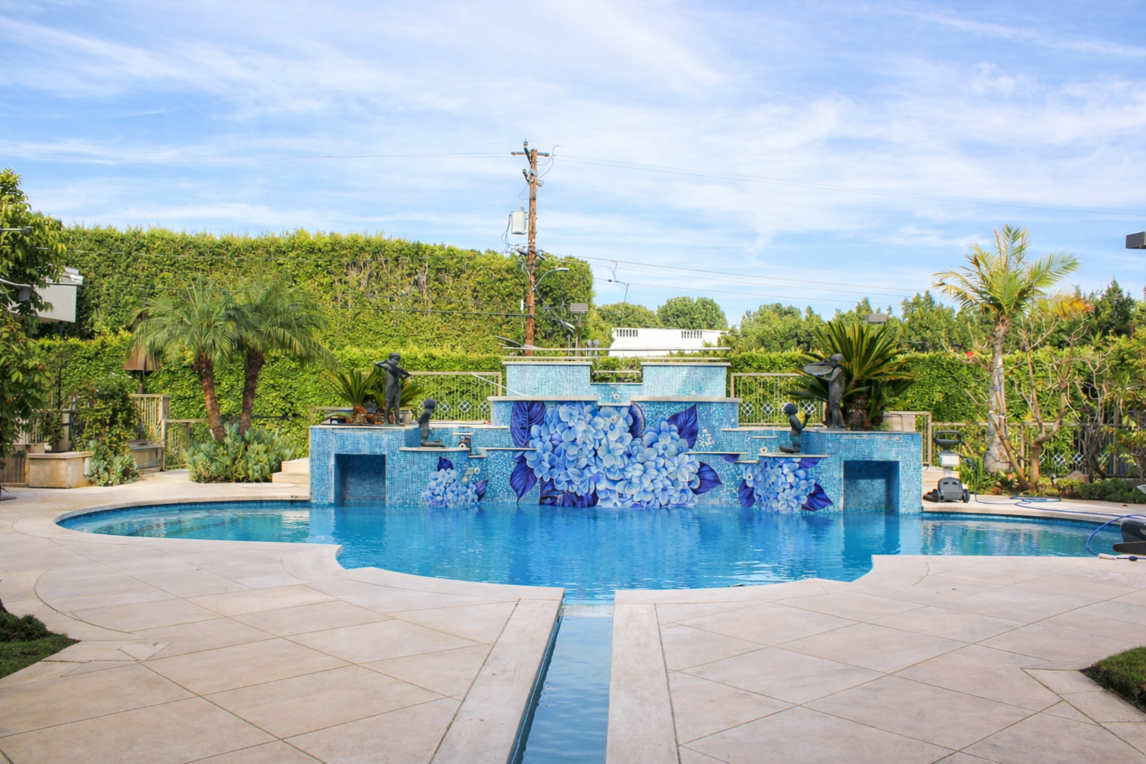 The image shows a landscaped pool area featuring a mosaic waterfall and lush greenery surrounding the water.