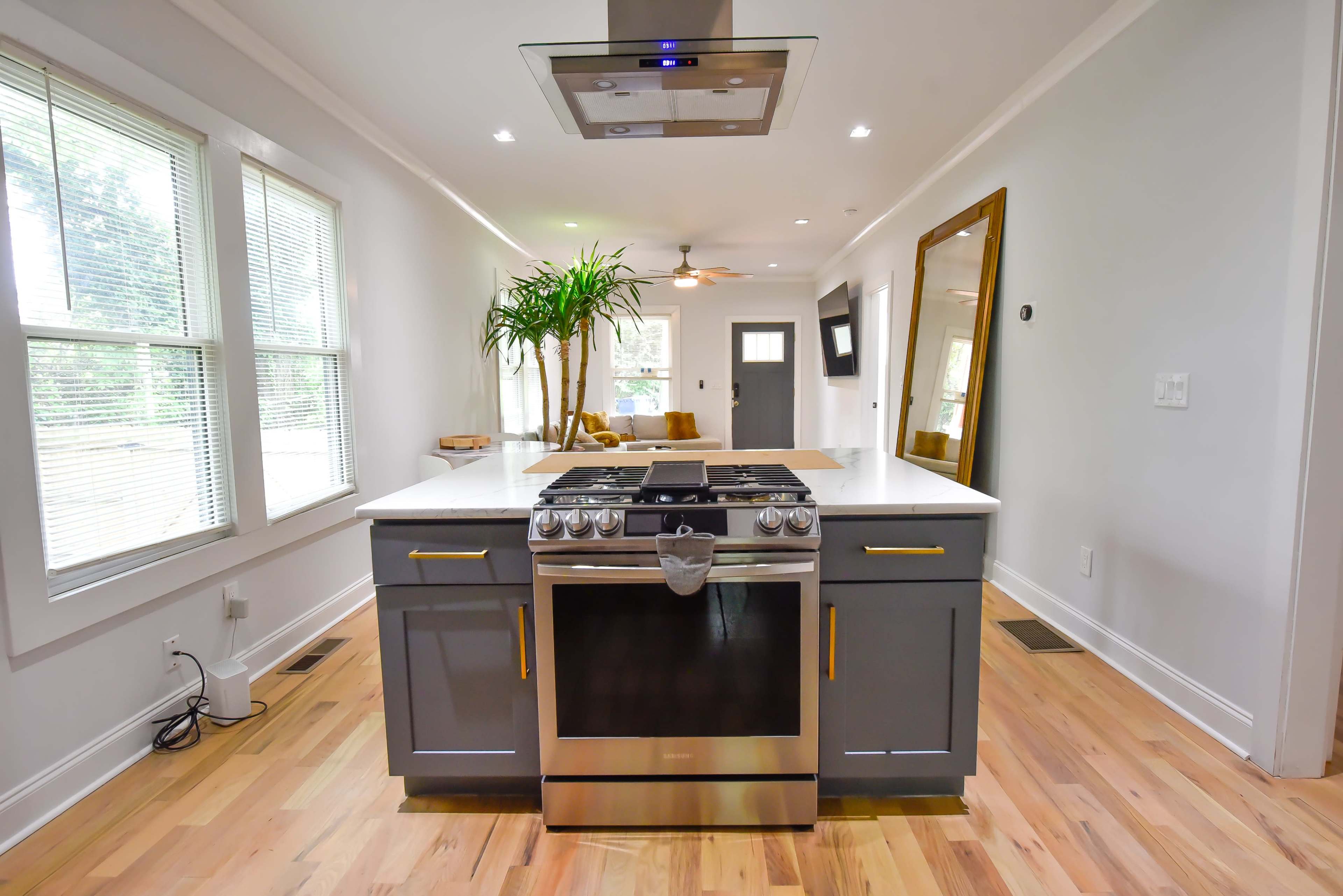 A modern kitchen featuring a central island with a stove, surrounded by light gray cabinetry and ample natural light from large windows.
