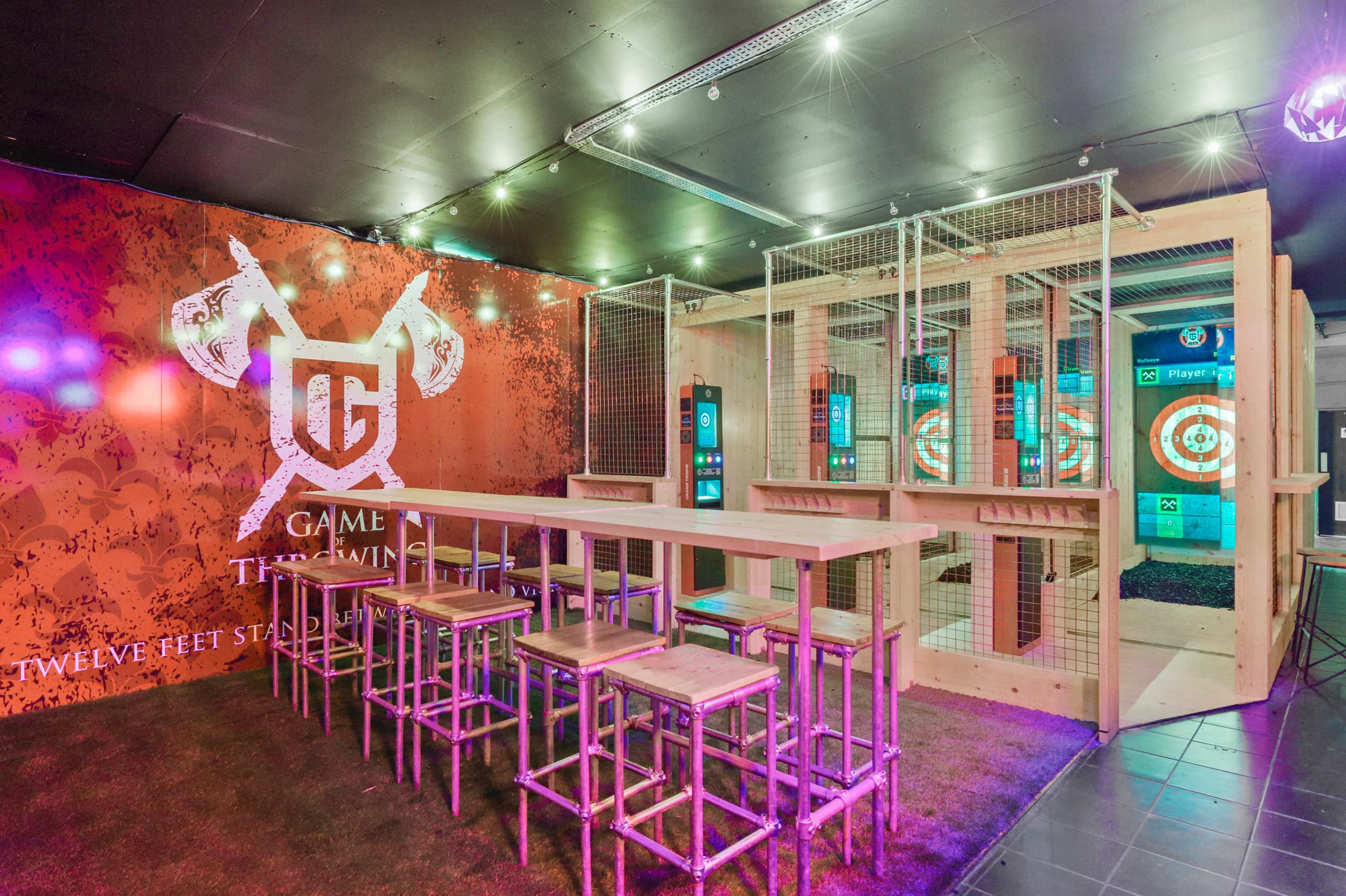 A sports venue featuring a bar area with high stools and a section for dart games enclosed in wooden fencing.