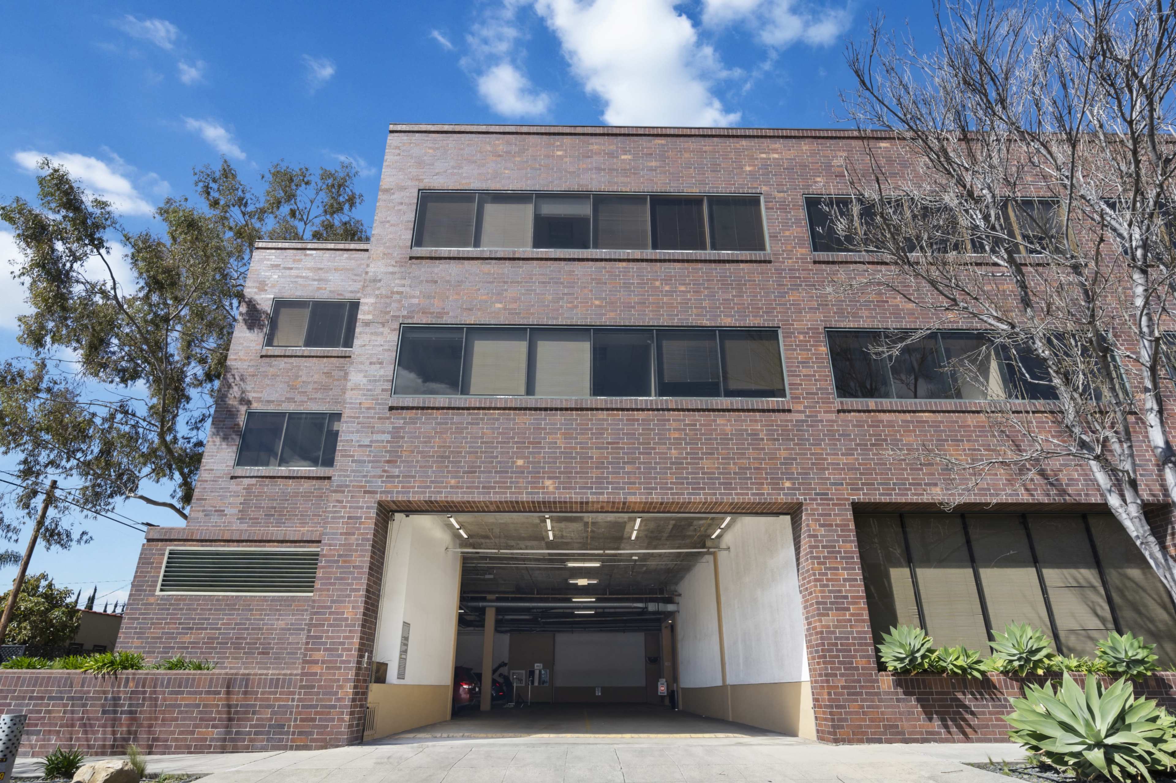 The image shows a modern brick building with large windows and an entrance to a parking area.