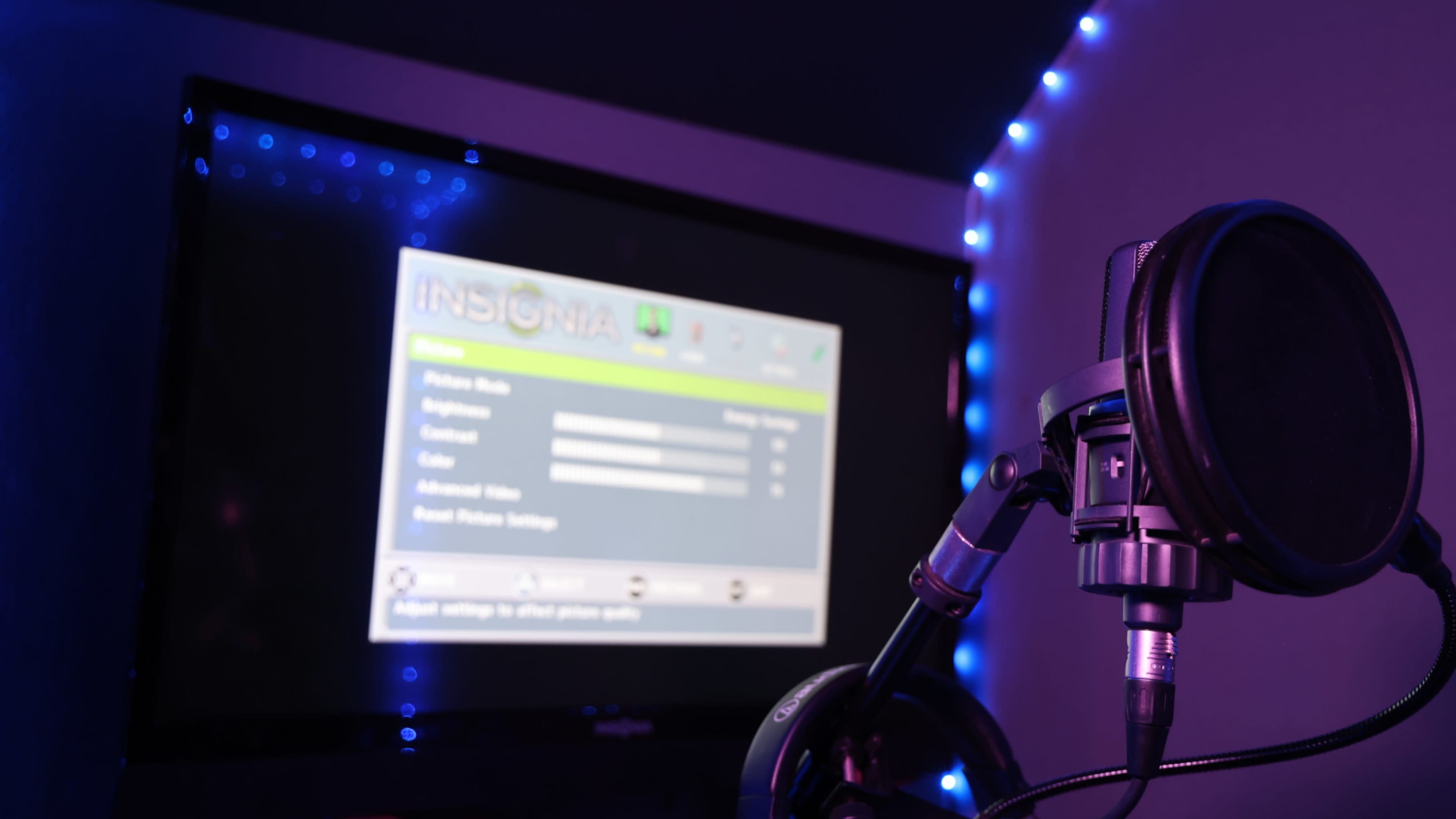 A microphone is positioned in front of a screen displaying settings for a device labeled "INSIGNIA," with blue lights illuminating the surrounding area.