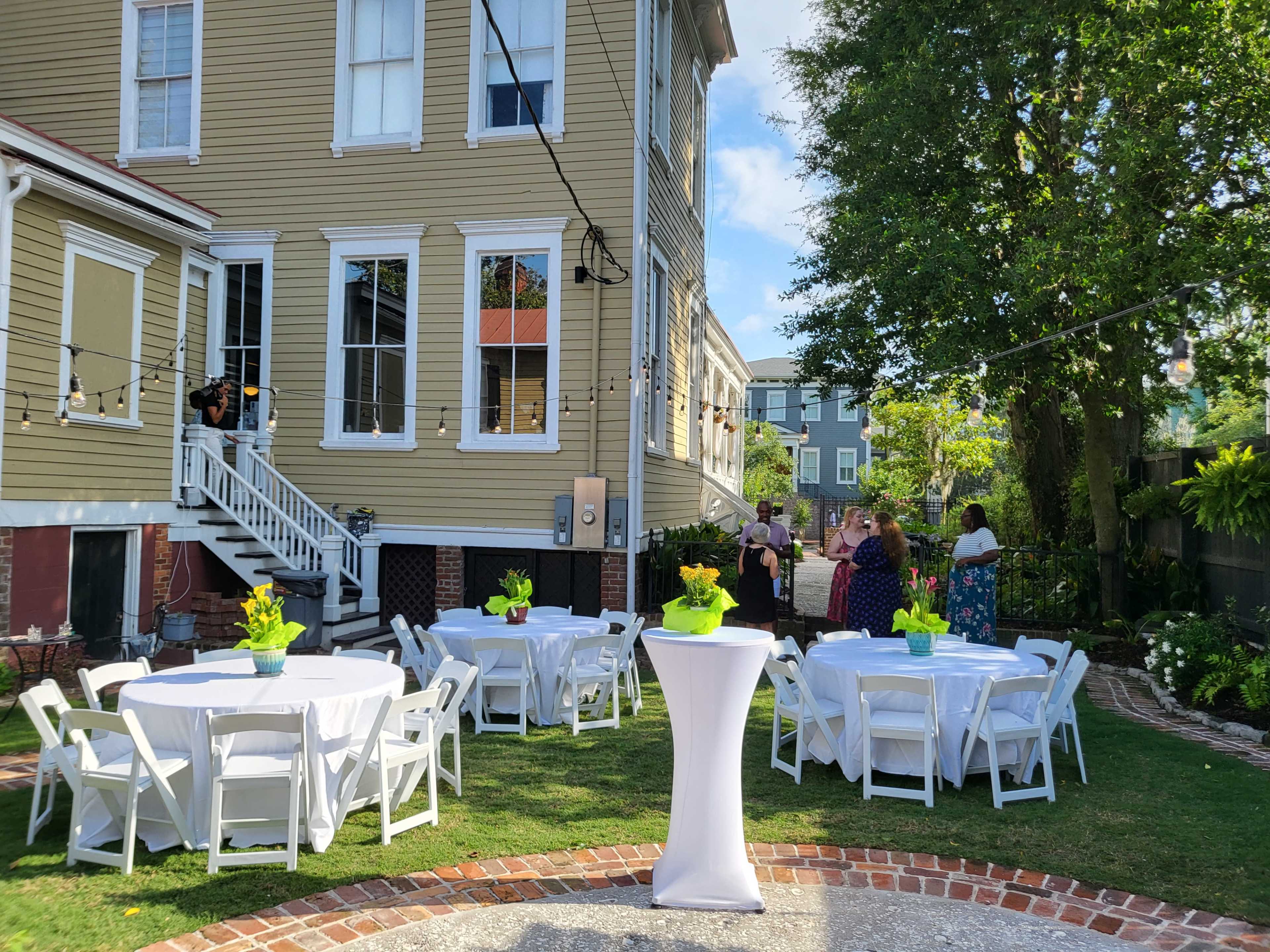 An outdoor event setup with circular tables and chairs arranged neatly on a lawn next to a large house.