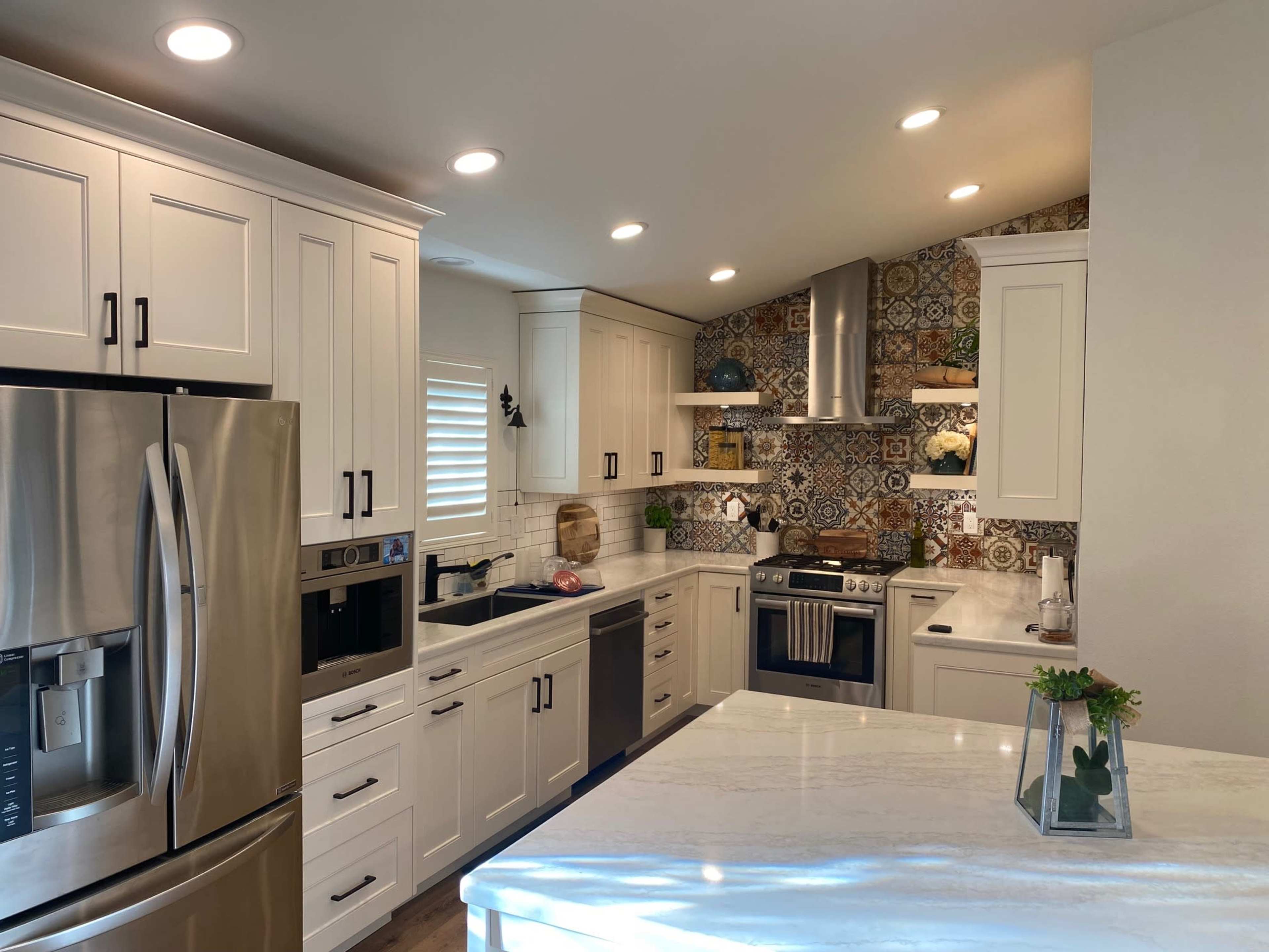 A modern kitchen features white cabinetry, stainless steel appliances, and colorful tile accents on the wall.