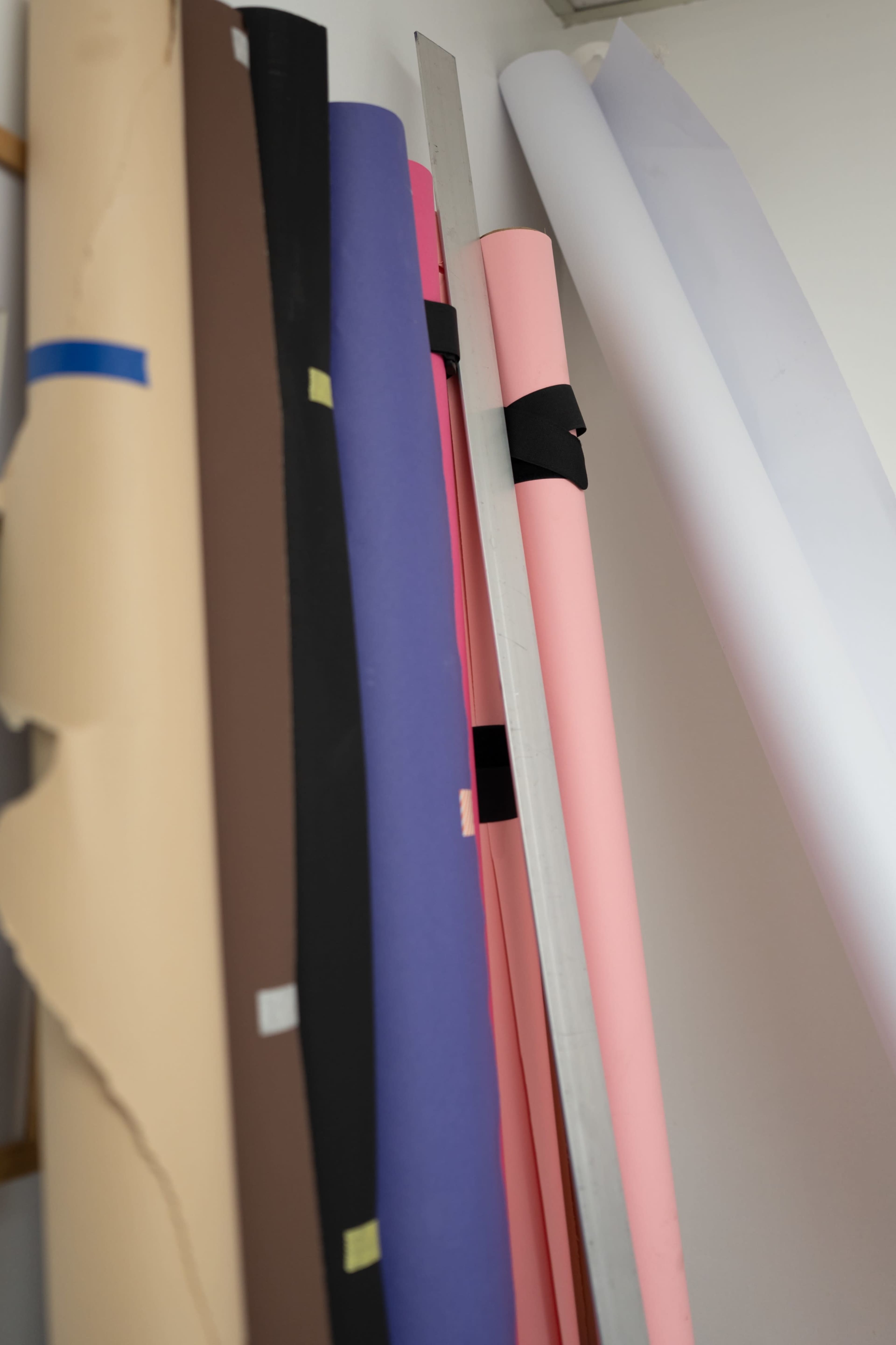 A collection of rolled paper sheets in various colors is neatly stored against a wall, with a metal ruler resting among them.