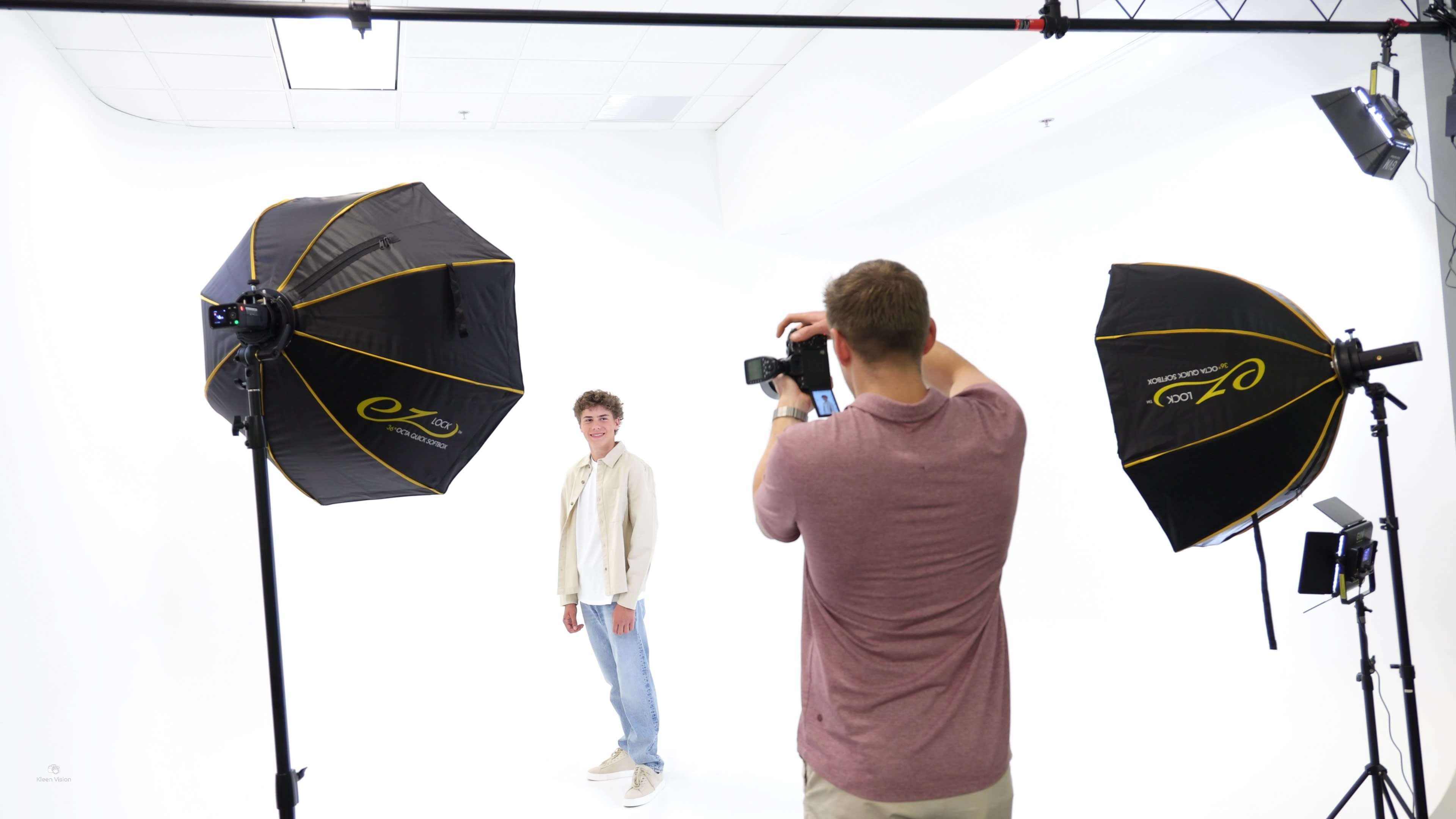 A photographer is capturing a portrait of a model in a studio setting with two softbox lights illuminating the scene.