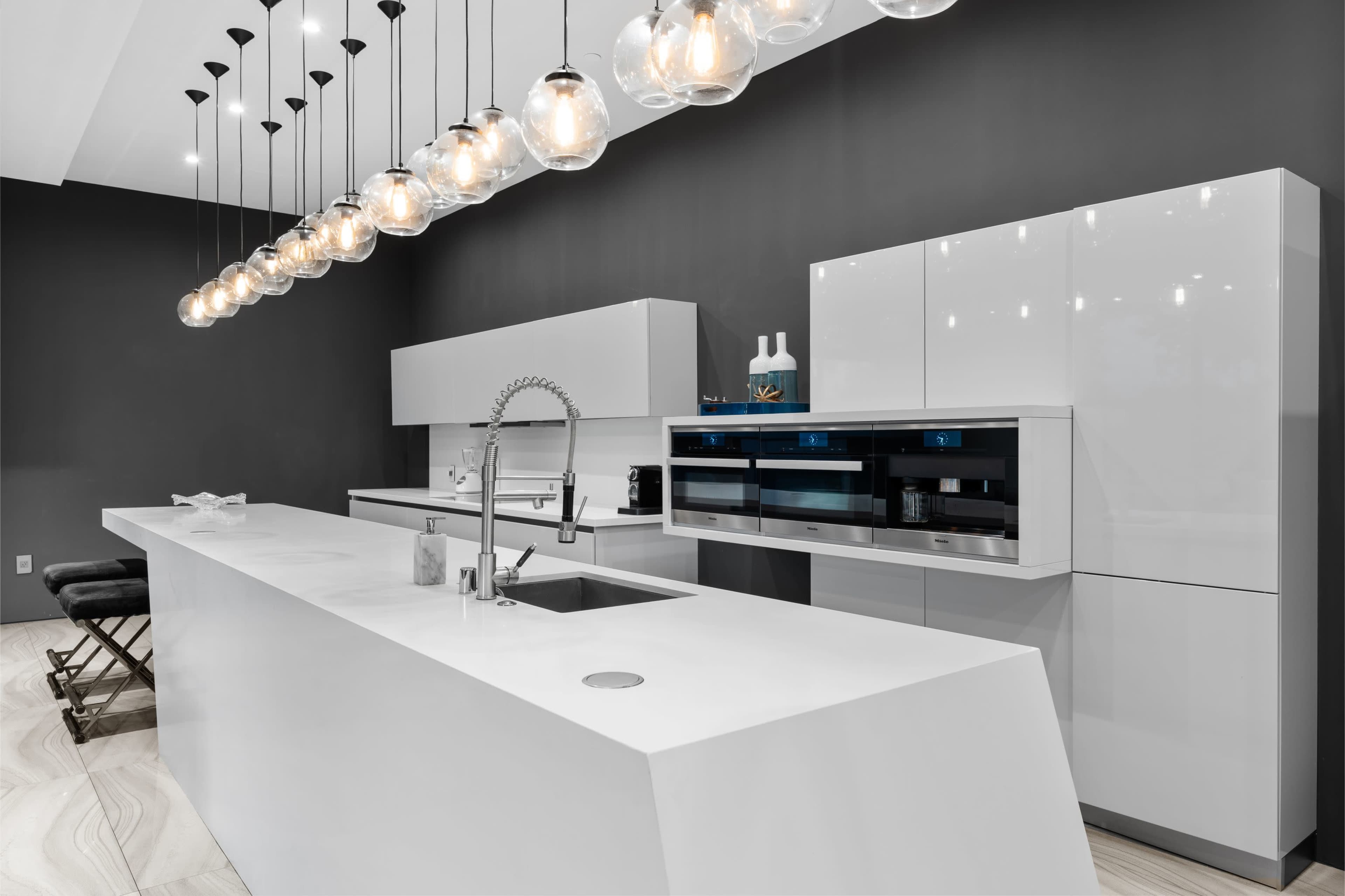 The image shows a modern kitchen with a sleek white island, shiny cabinetry, and pendant lights hanging from the ceiling.