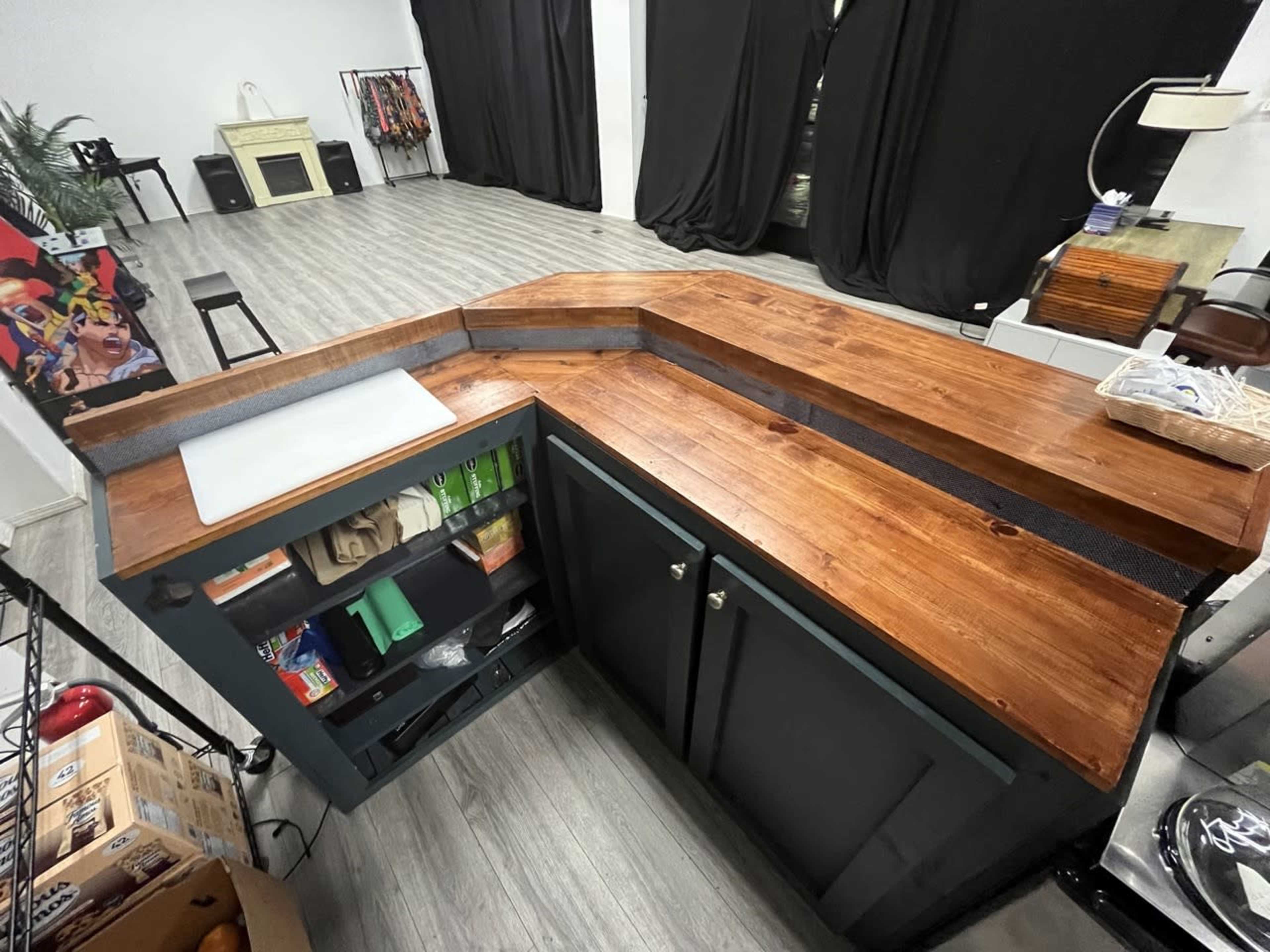 A wooden countertop with a unique design, situated in a spacious room with dark curtains and various items in the background.