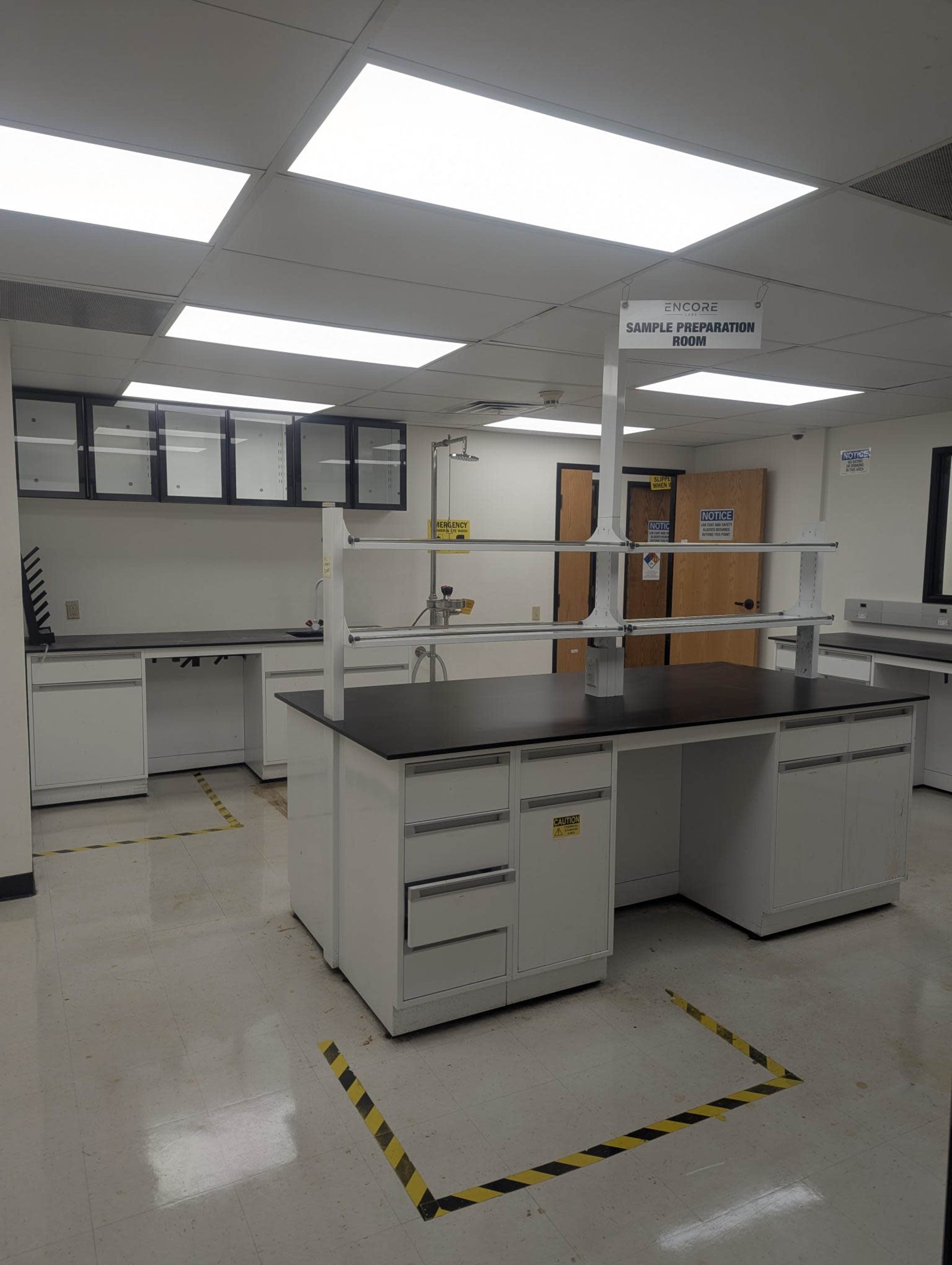 The image shows a clean laboratory space with workbenches, storage cabinets, and safety markings on the floor.