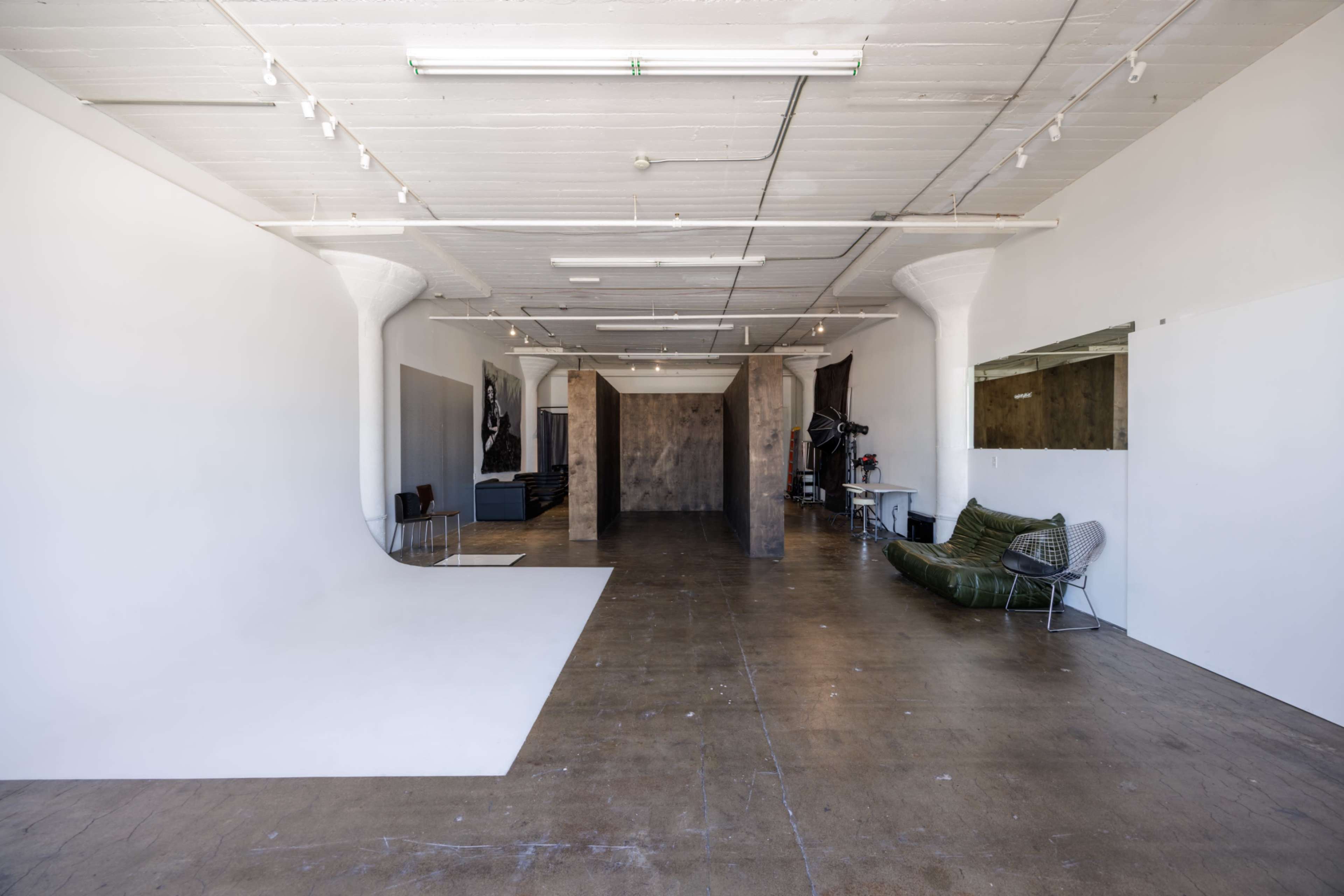 The image shows a spacious, well-lit studio with a plain white backdrop on one side and various furniture arrangements, including a green sofa, on the other.