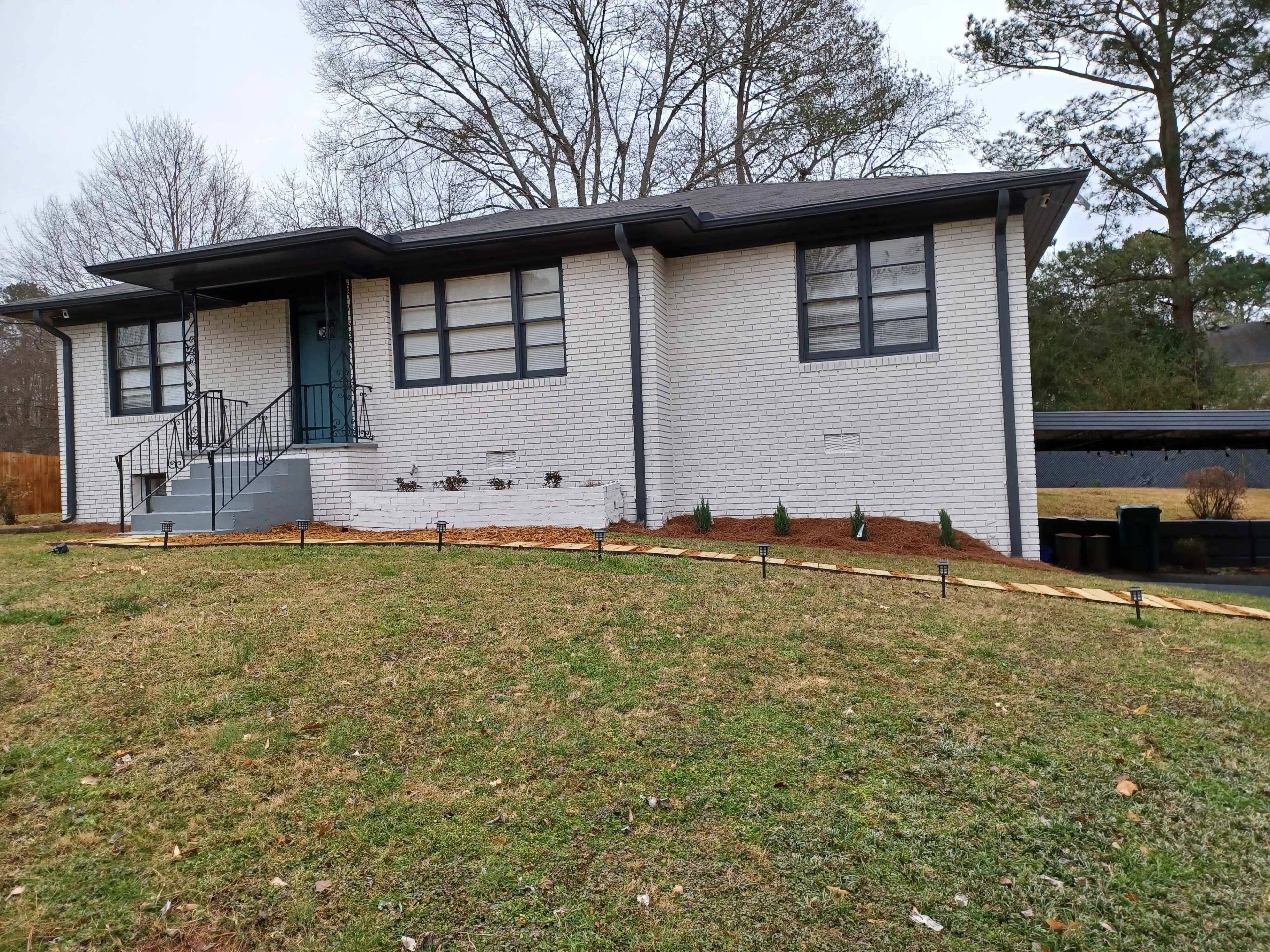 A single-story white brick house with a dark roof and a front staircase sits on a gently sloping lawn.