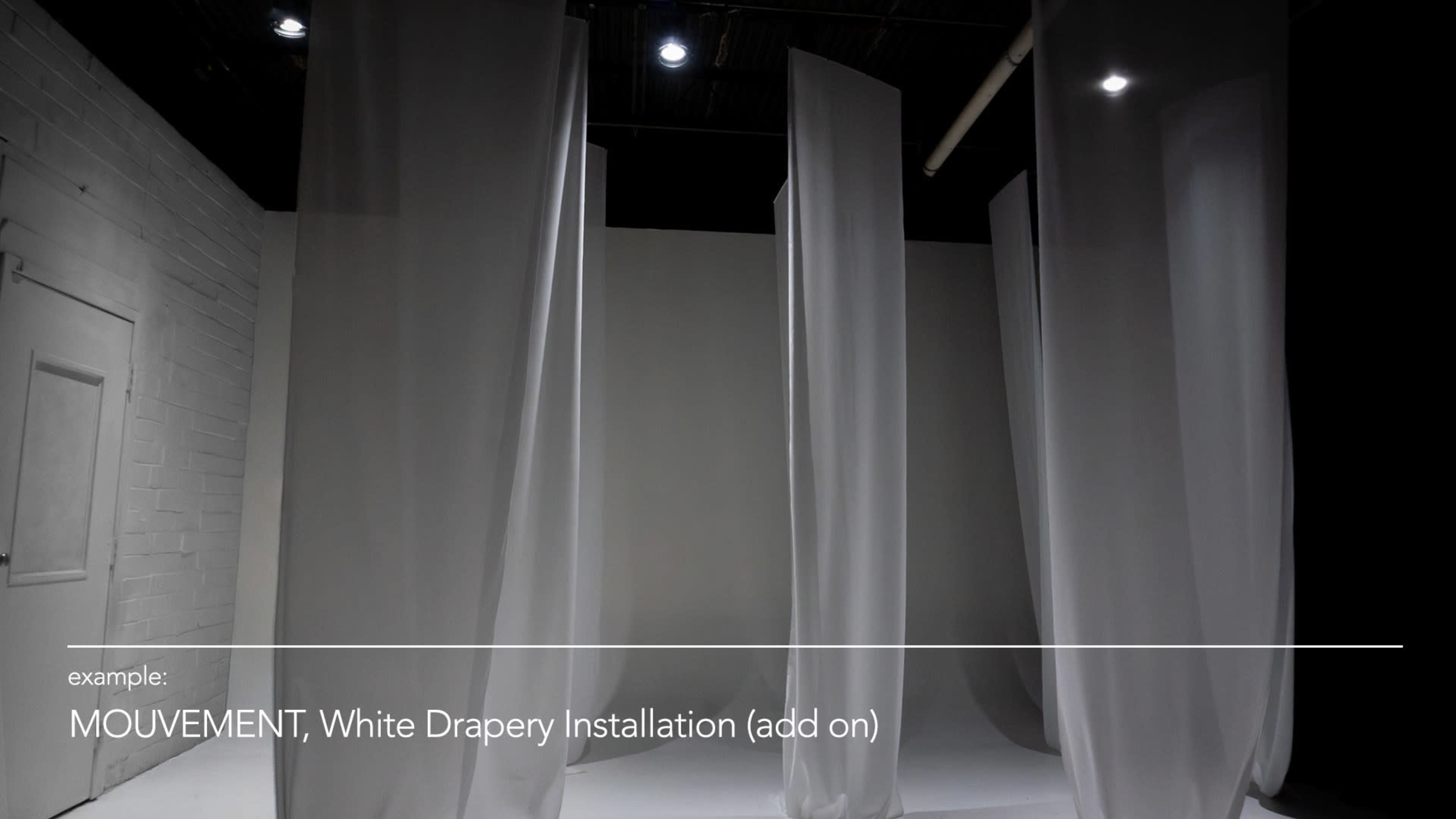 The image depicts a minimalist art installation featuring several tall white drapery panels arranged in an open space.