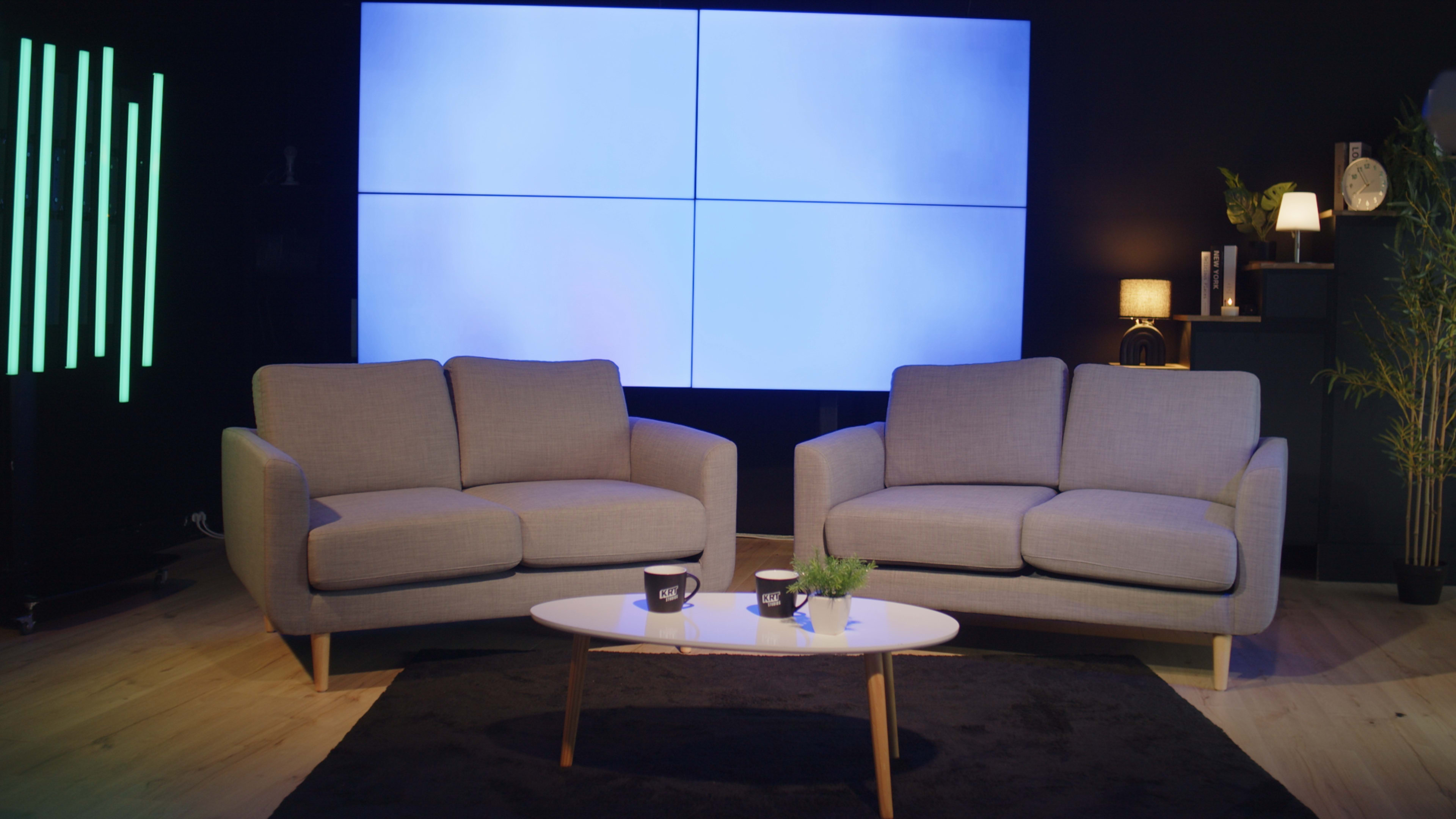 The image shows a modern living space with two gray sofas facing a coffee table in front of a large screen divided into four panels.