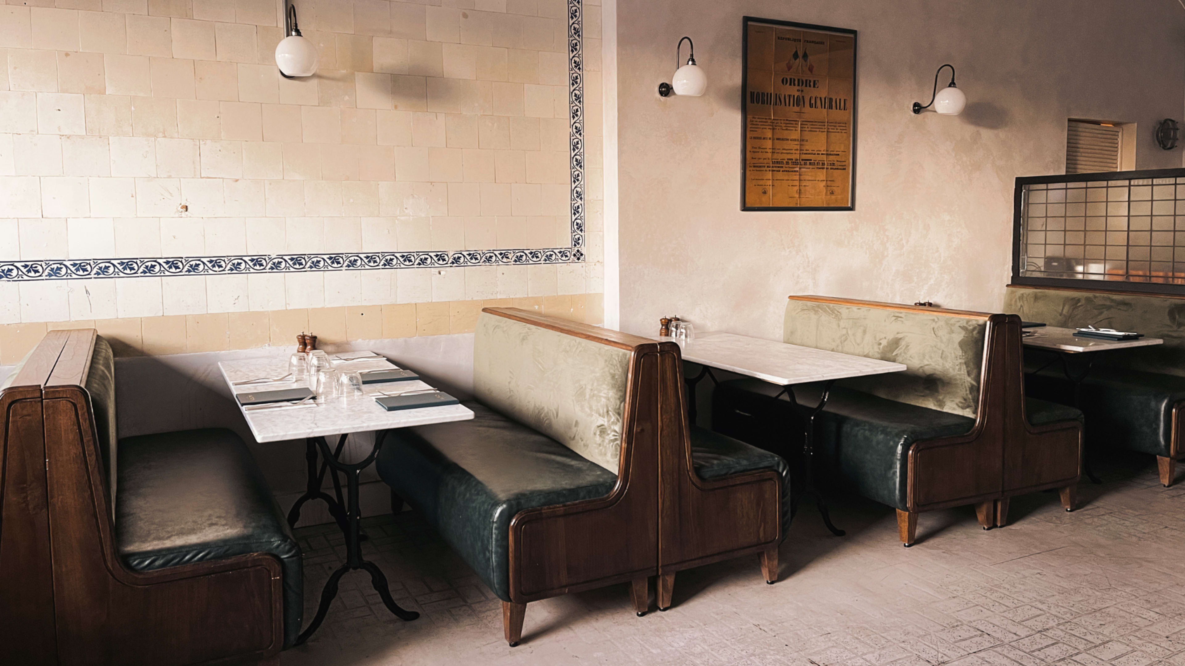 A restaurant interior with wooden booth seating, marble-topped tables, and a tiled wall adorned with a framed vintage poster.