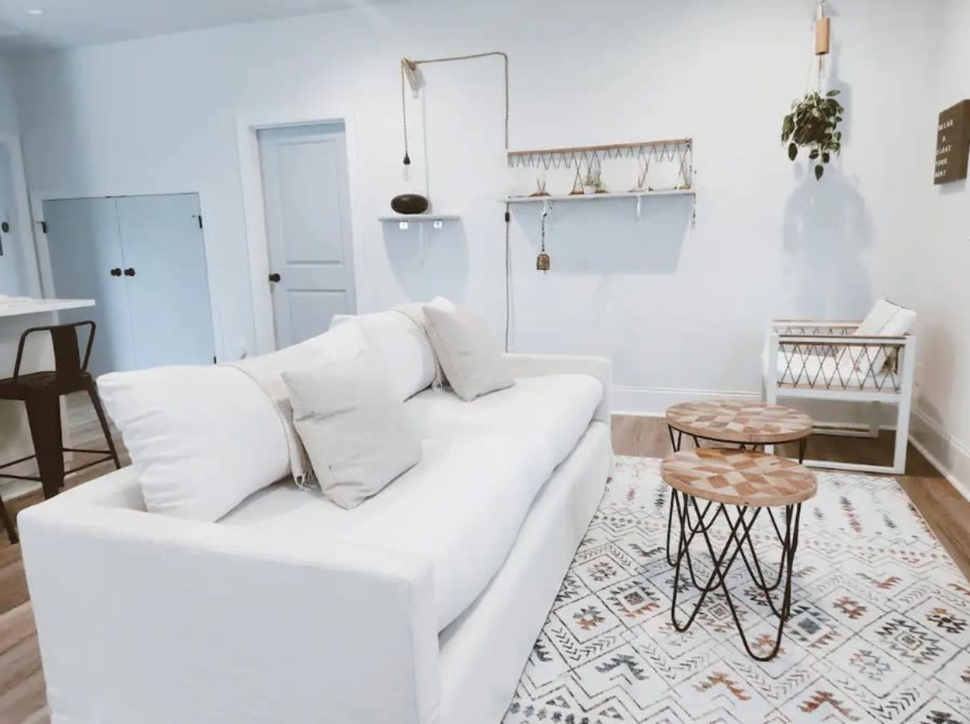 A modern living room with a white sofa, two small wooden tables, and light-colored walls, accented by minimal decorative elements.