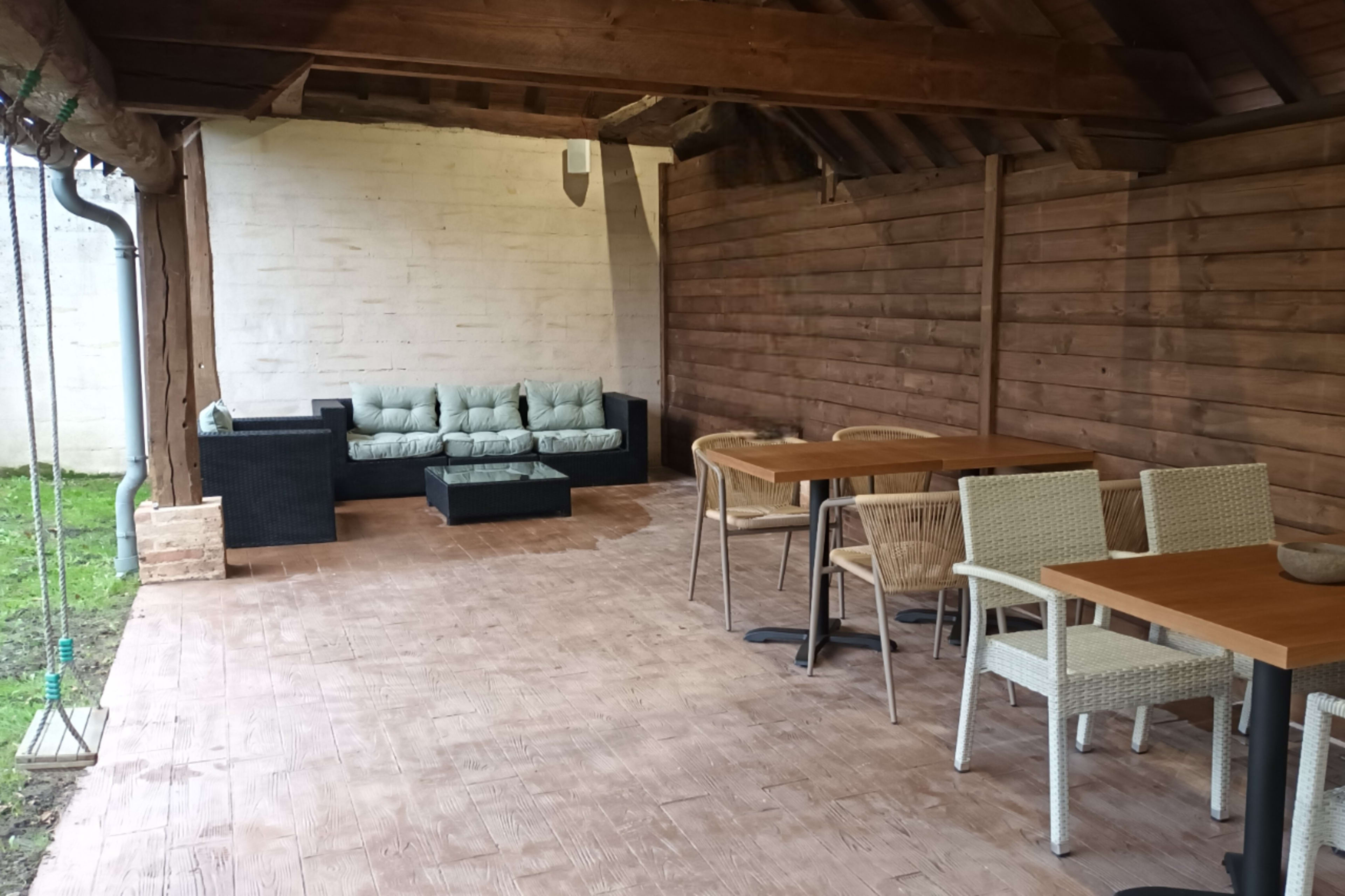 The image shows a covered outdoor seating area with a couch, a coffee table, and two dining tables with chairs.