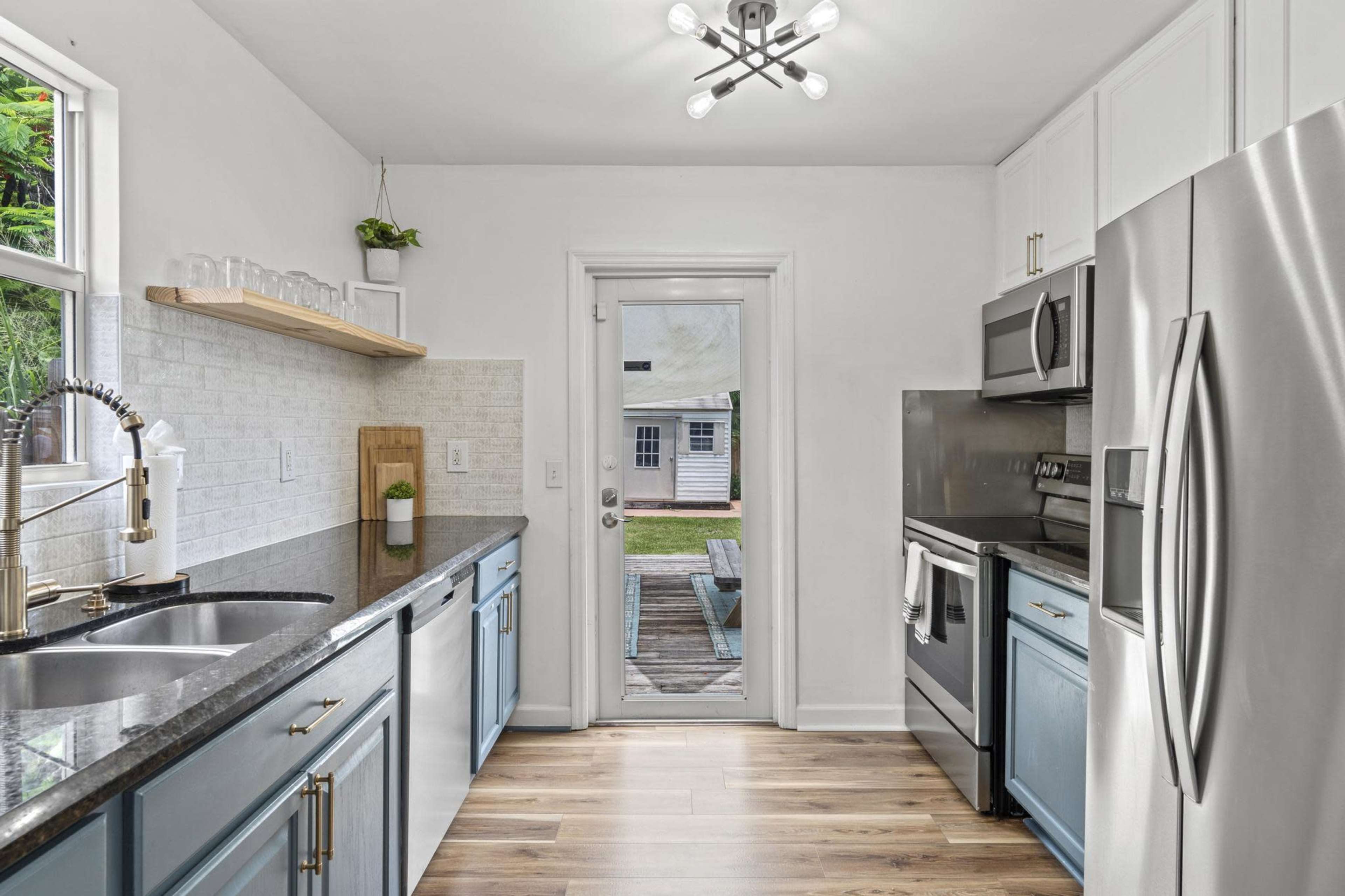 A modern kitchen with blue cabinetry, stainless steel appliances, and a doorway leading to an outdoor deck.