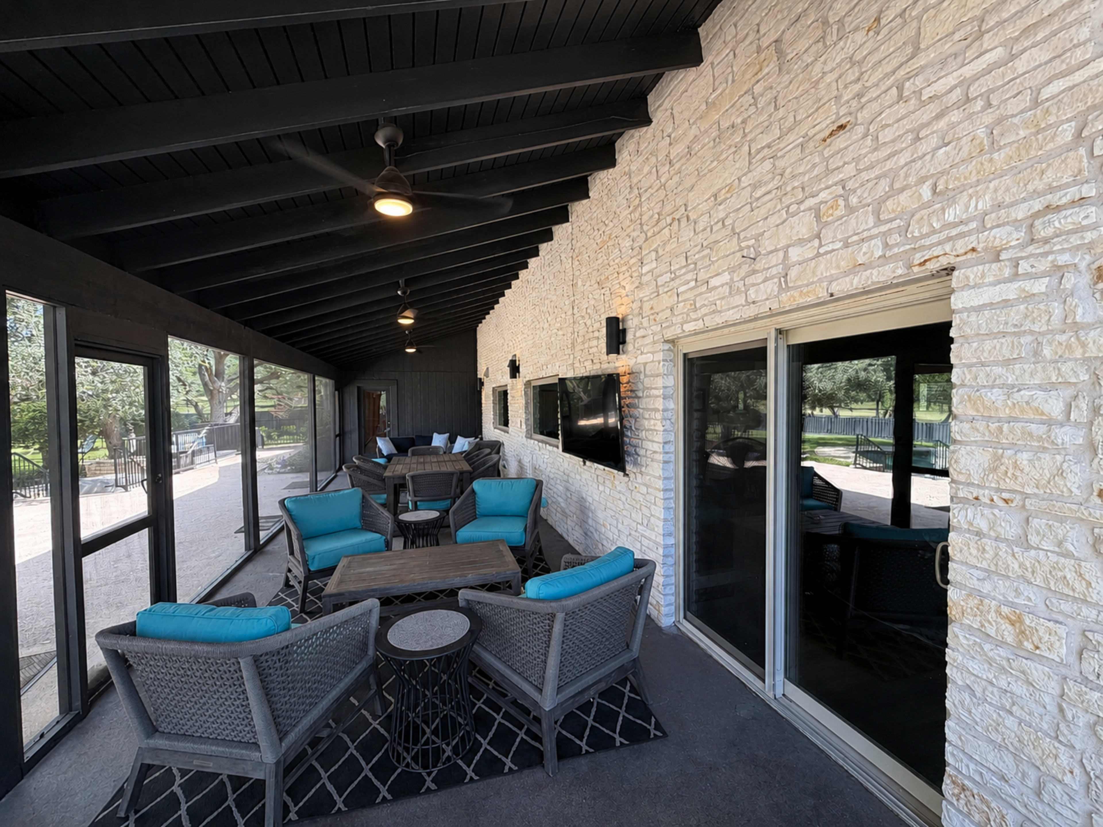 The image shows a spacious sunroom with stone walls, large windows, and comfortable seating arranged around a central coffee table.