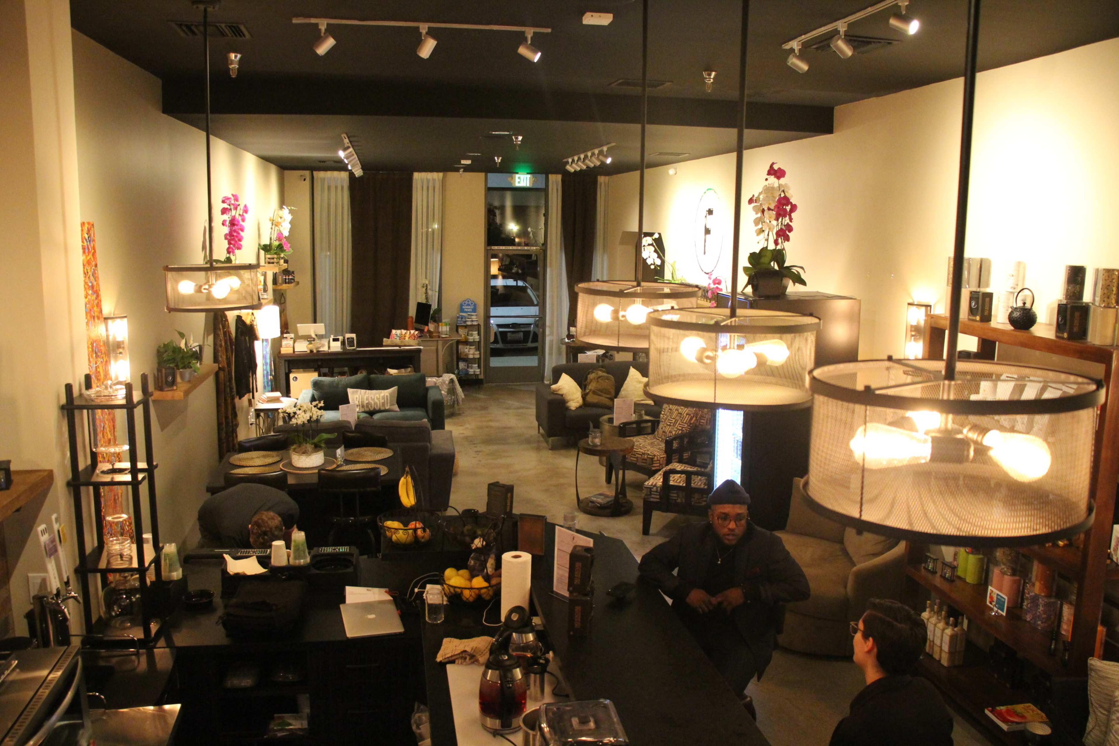 A stylish café interior with seating arrangements, a bar area, and decorative plants, illuminated by pendant lights.