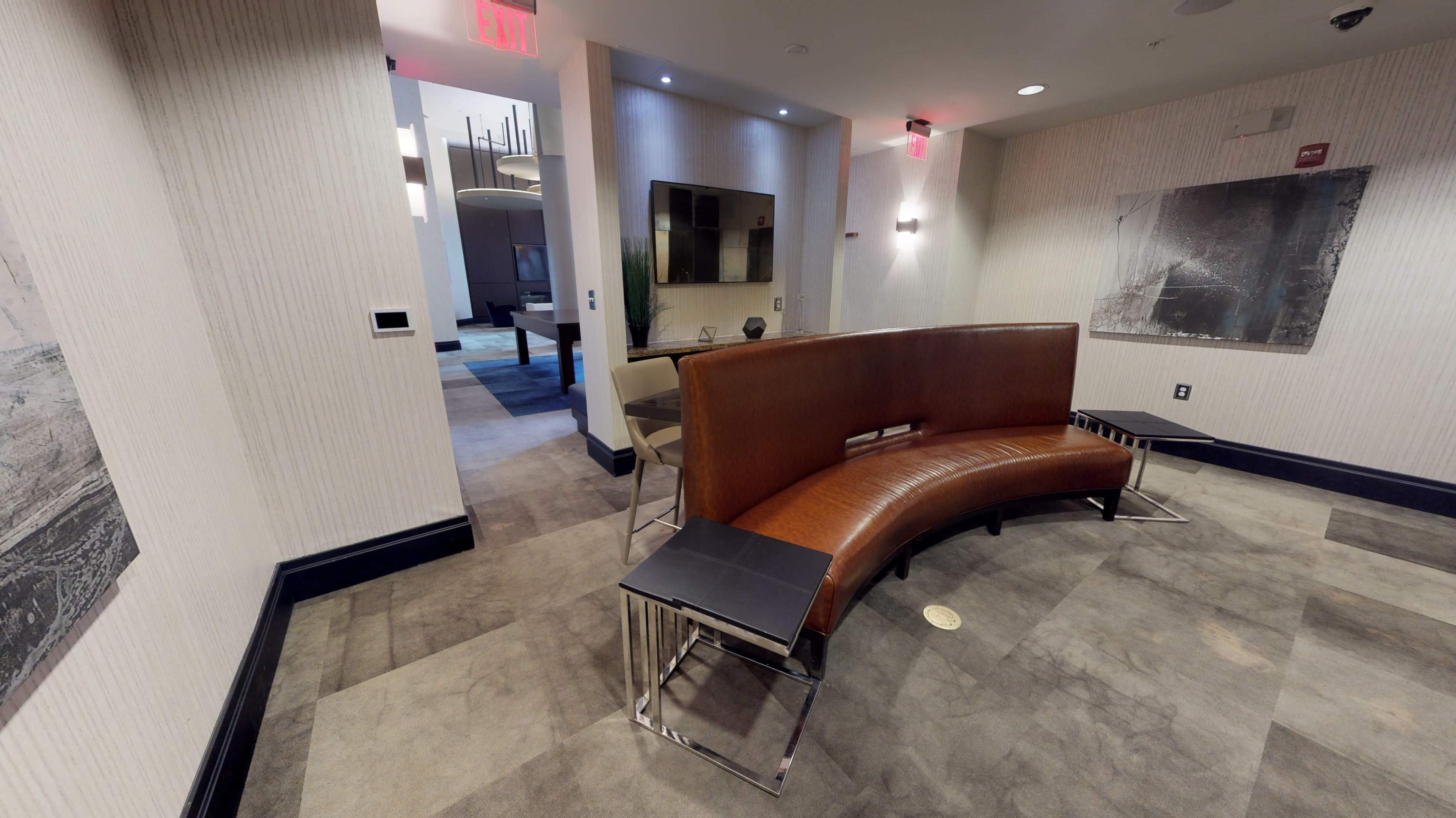 A modern lobby area with a curved brown bench and a wall-mounted television in the background.