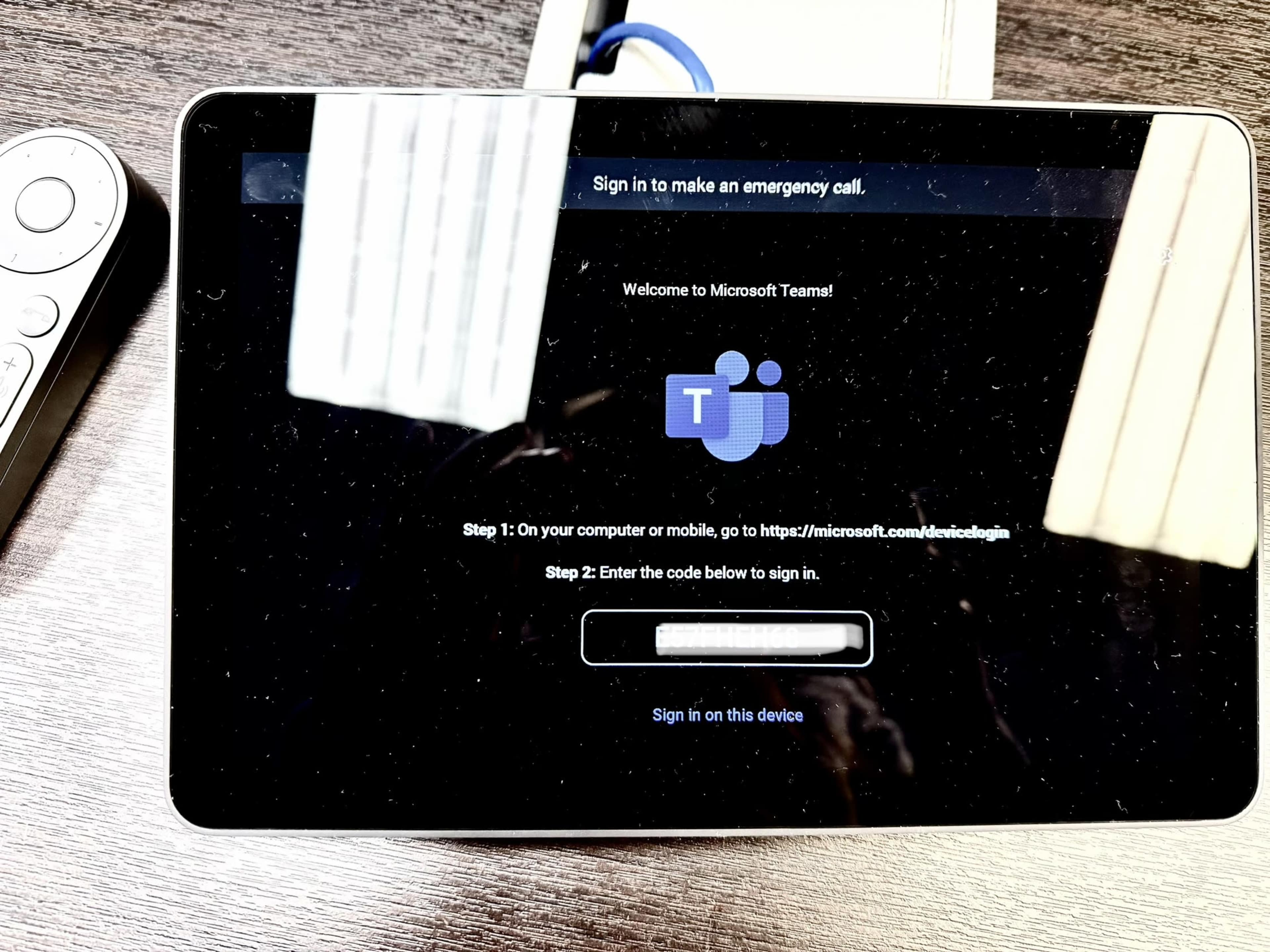 The image shows a tablet screen displaying a Microsoft Teams login page with instructions for signing in, and the device is placed on a wooden surface.