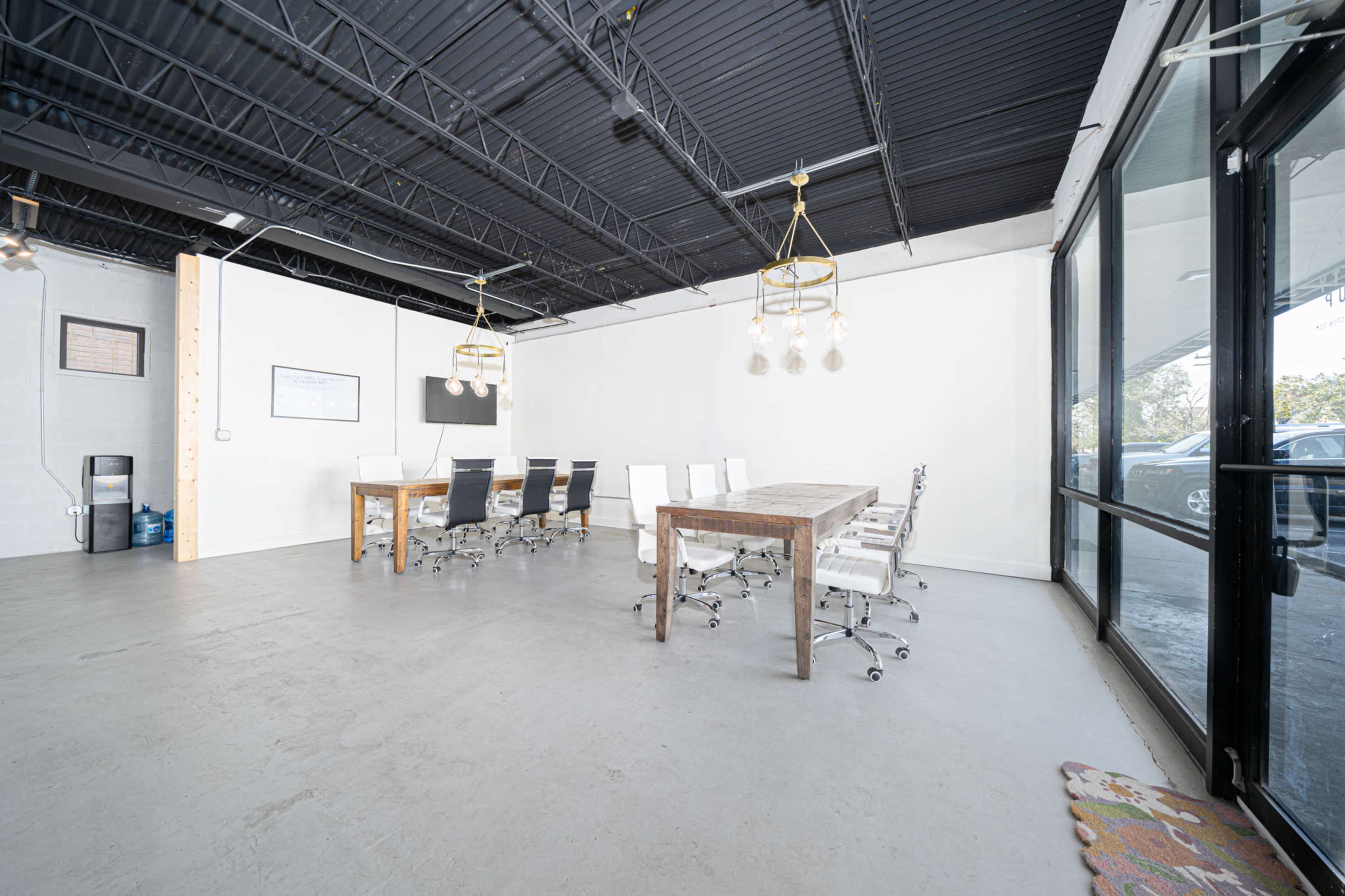 The image shows a modern conference room with a large wooden table surrounded by ergonomic chairs, and large windows allowing natural light.