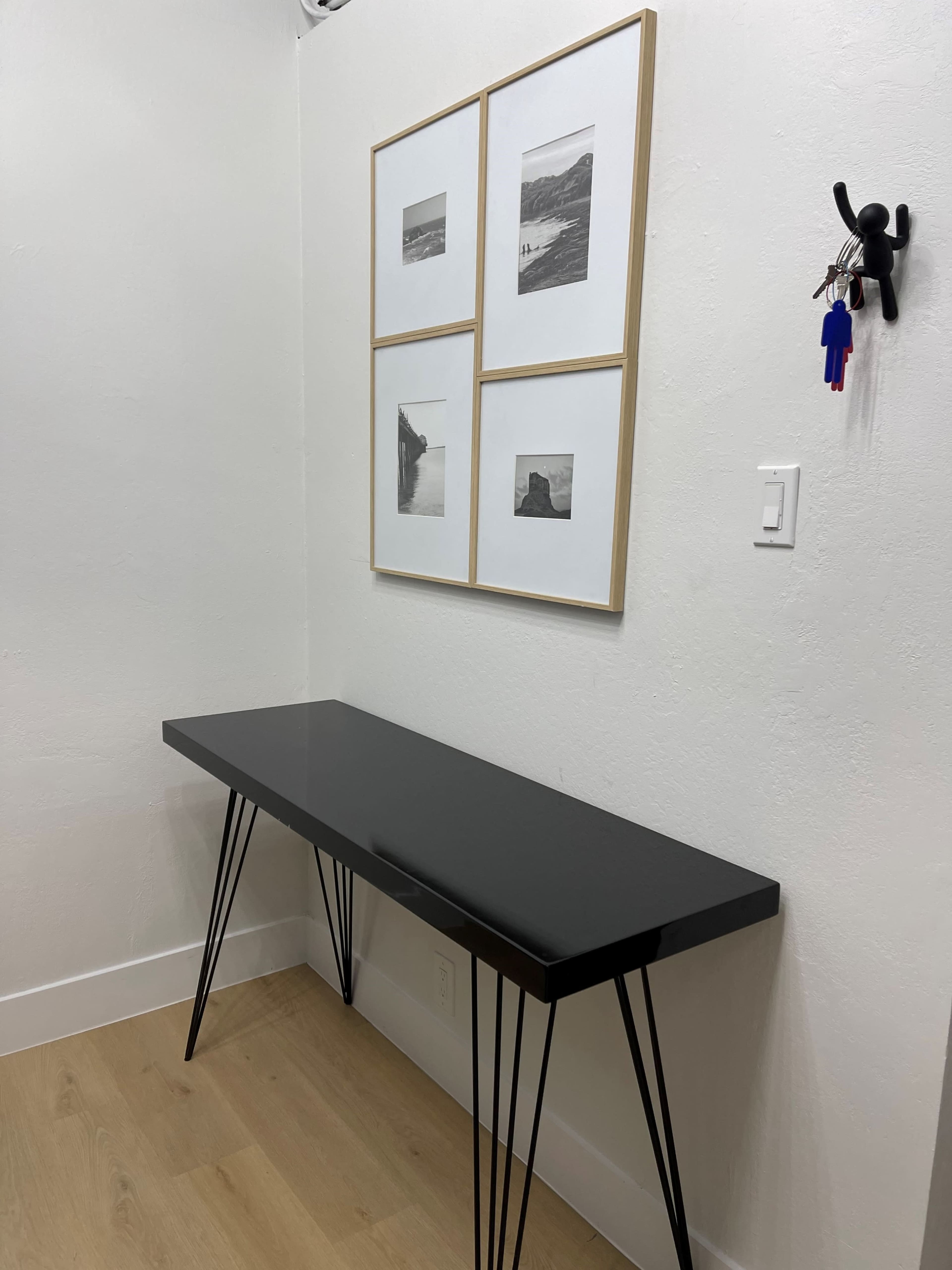 A black table with slender legs is placed against a white wall, adorned with four framed black-and-white photographs above it.