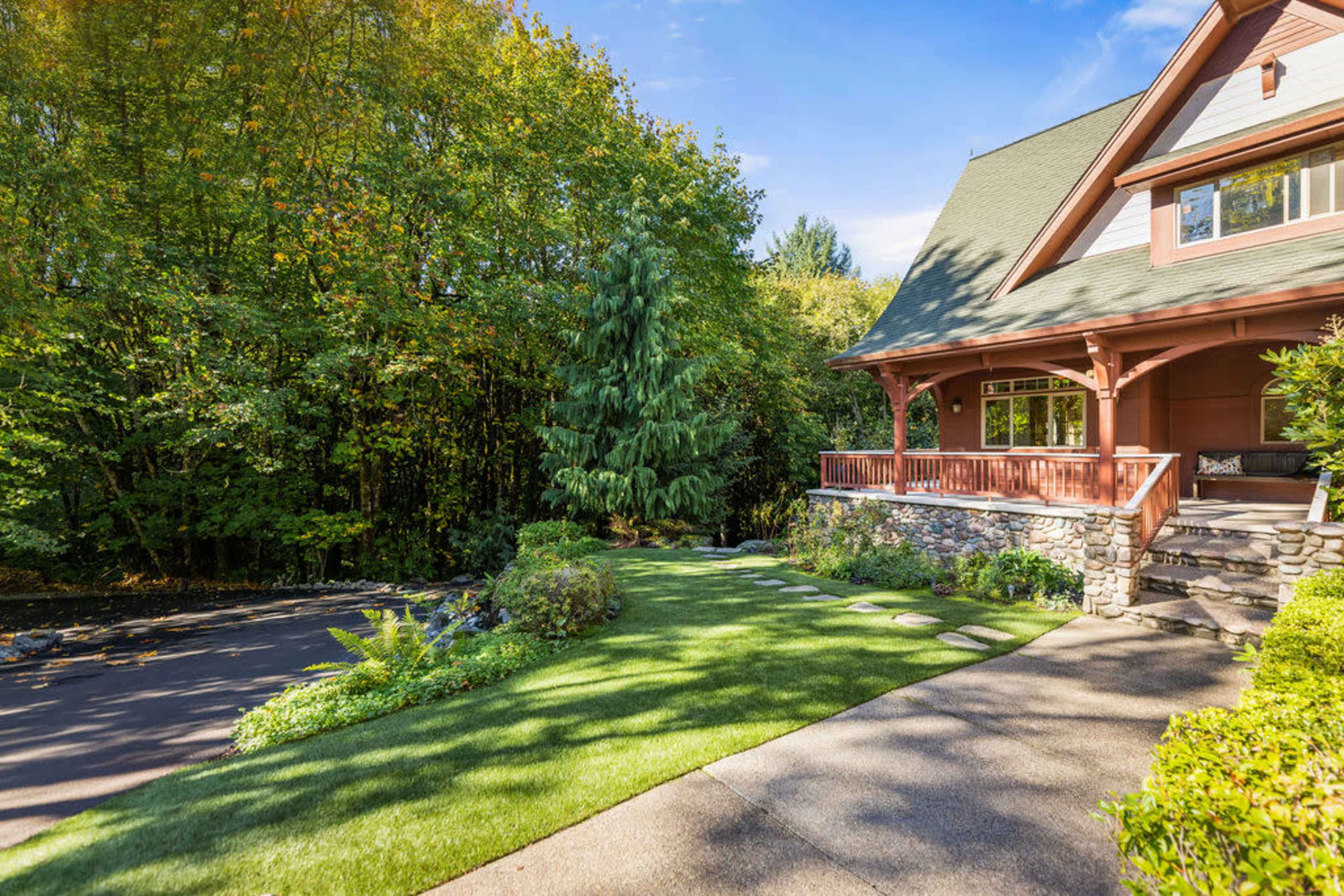 A two-story house with a porch is surrounded by lush greenery and a well-maintained lawn.