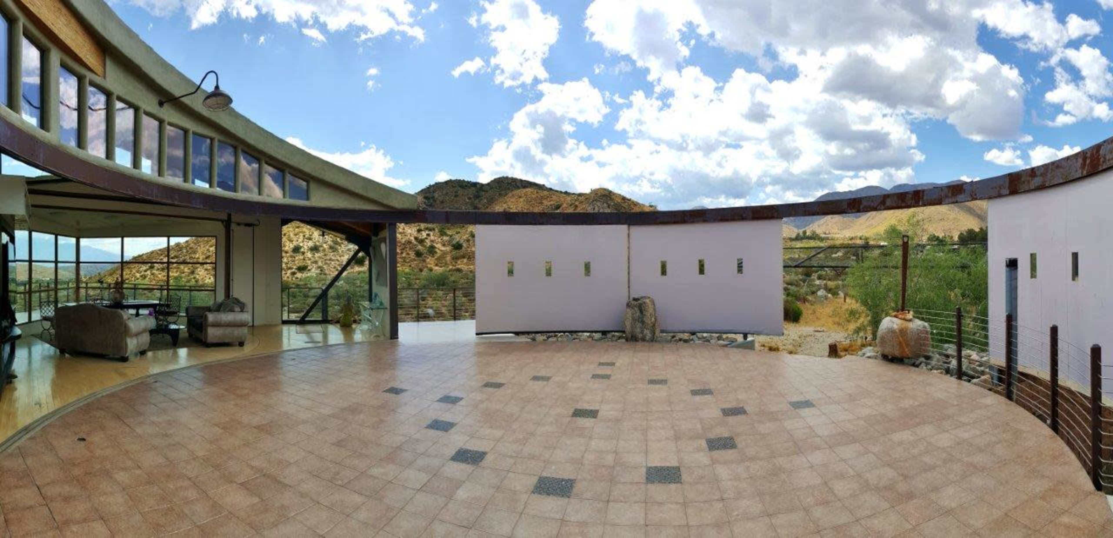 A modern circular structure with large windows, opening to a panoramic view of mountains under a partly cloudy sky.