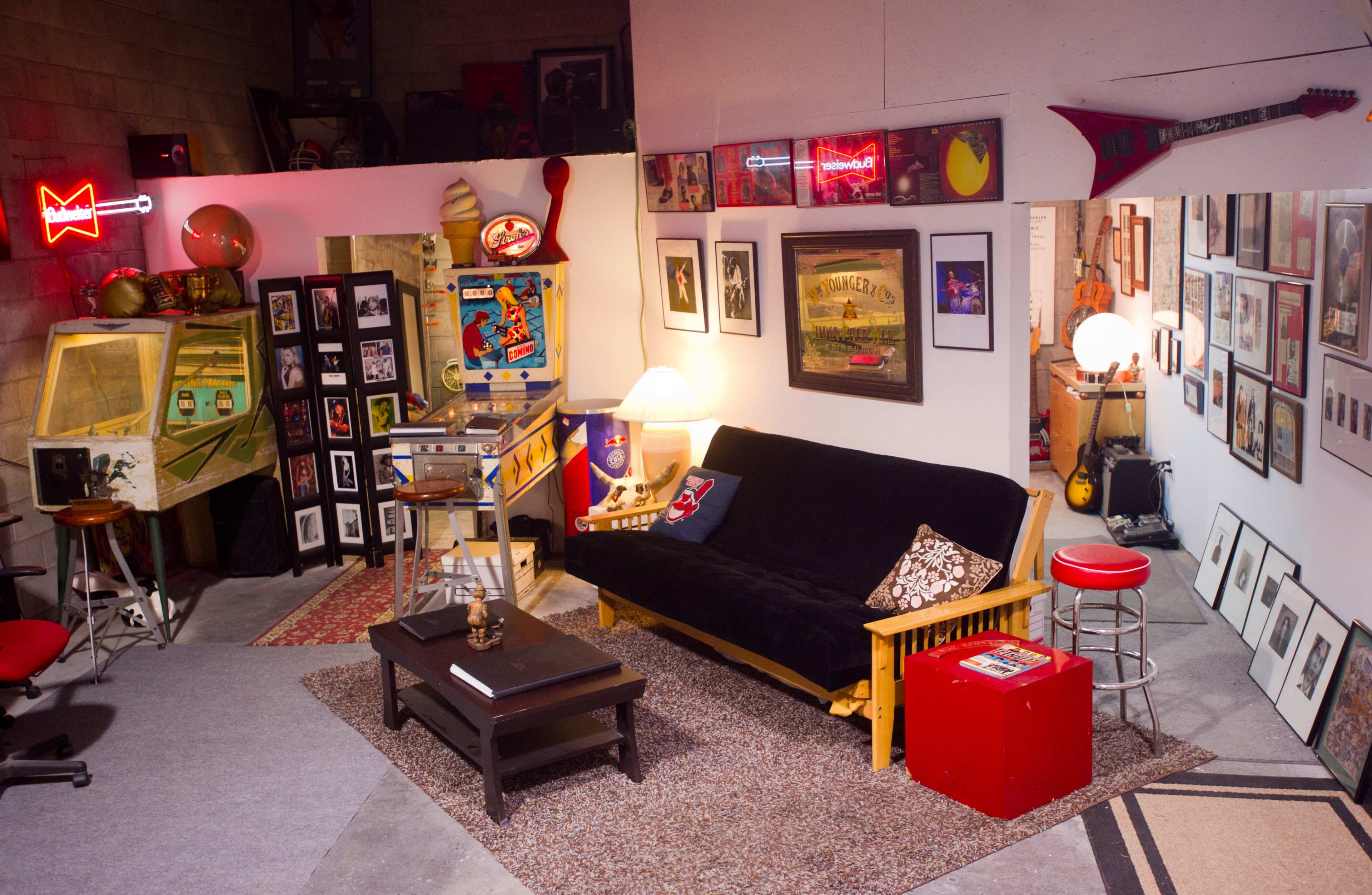 A cozy room with a black futon, a coffee table, posters on the walls, and a vintage jukebox illuminated by neon lights.
