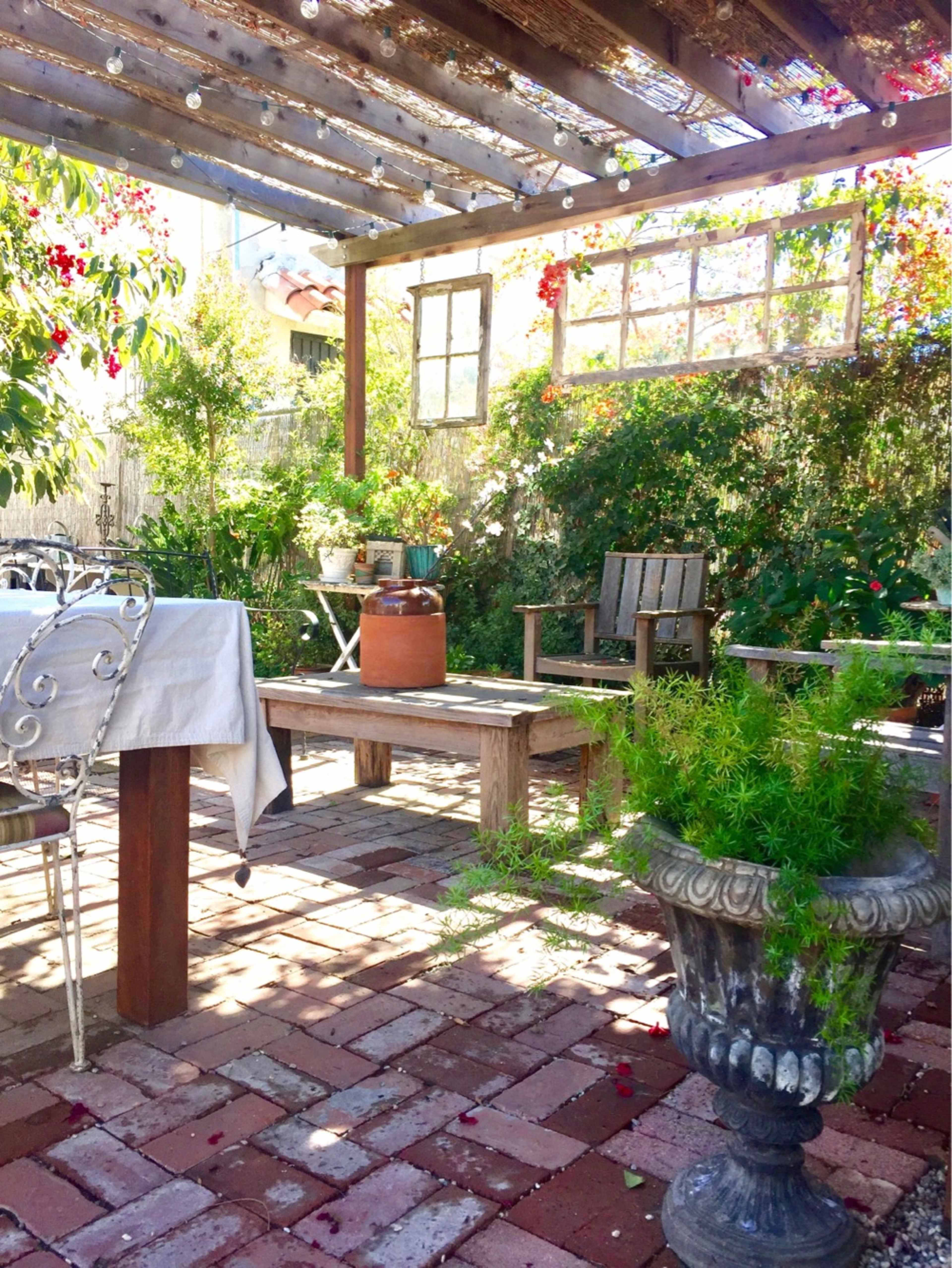 A rustic outdoor seating area with wooden furniture, potted plants, and string lights under a pergola.