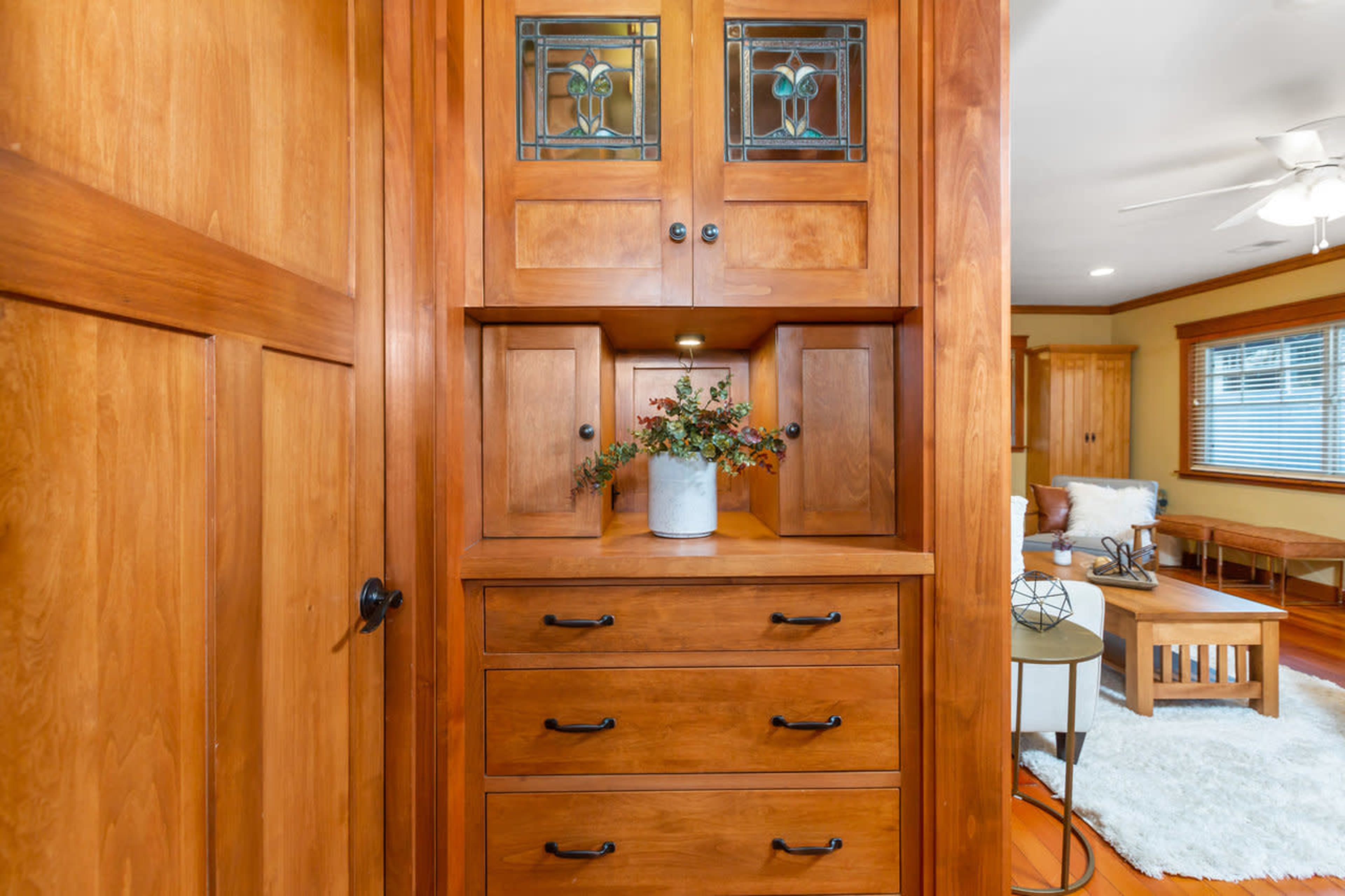 A wooden storage unit with glass-paneled doors and multiple drawers, positioned in a room featuring a seating area.
