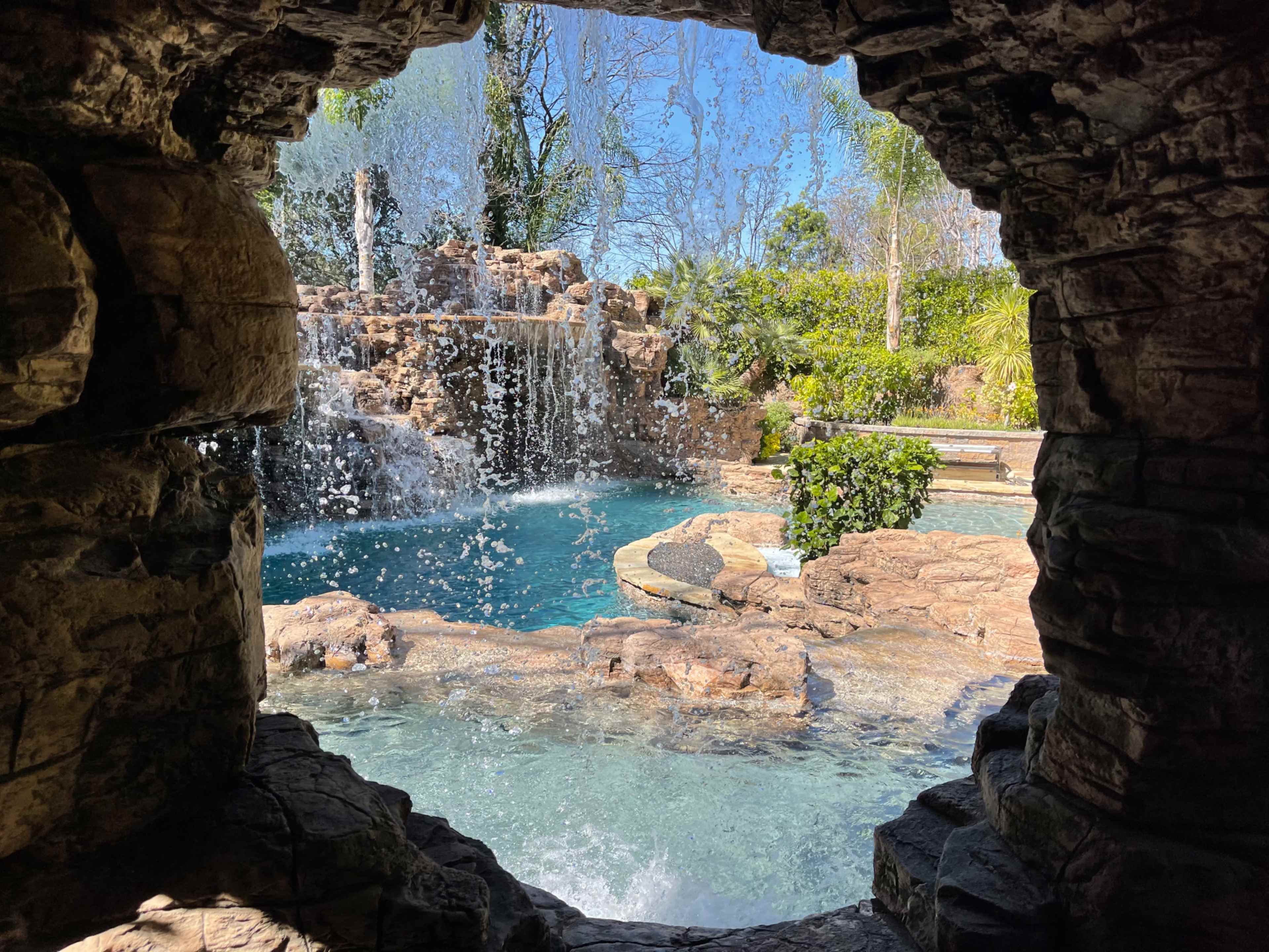 A view of a waterfall and swimming pool framed by a stone opening.