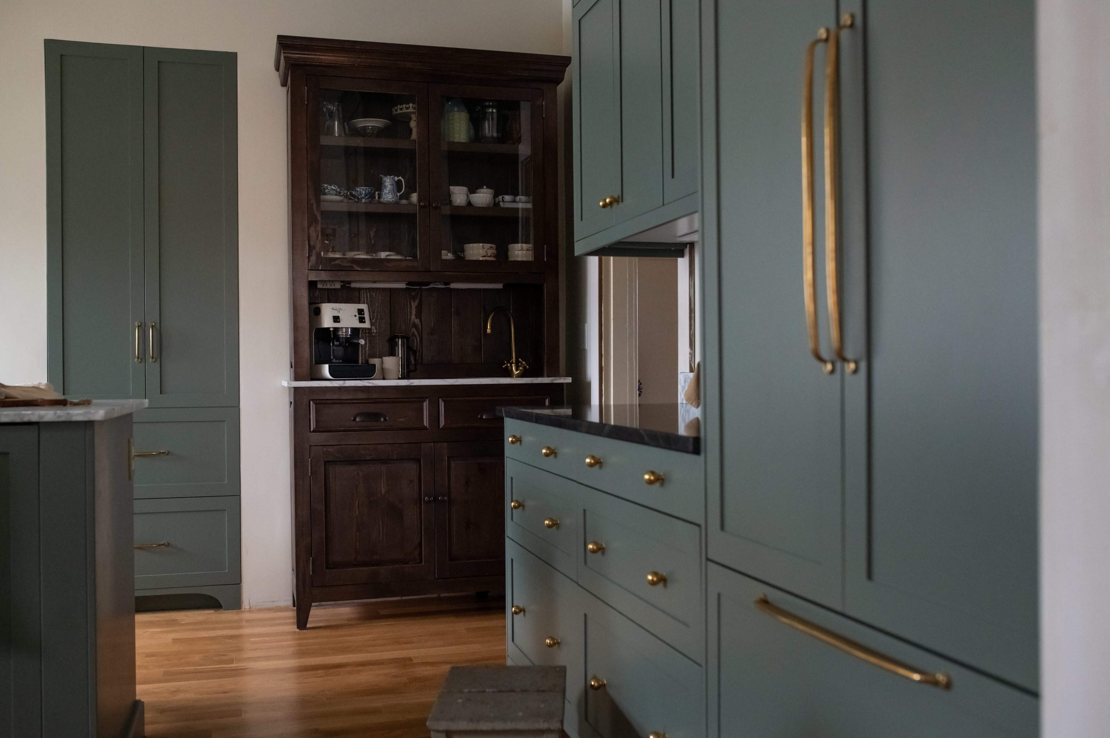 The image shows a kitchen with green cabinetry, wooden accents, and a coffee machine on a shelf.