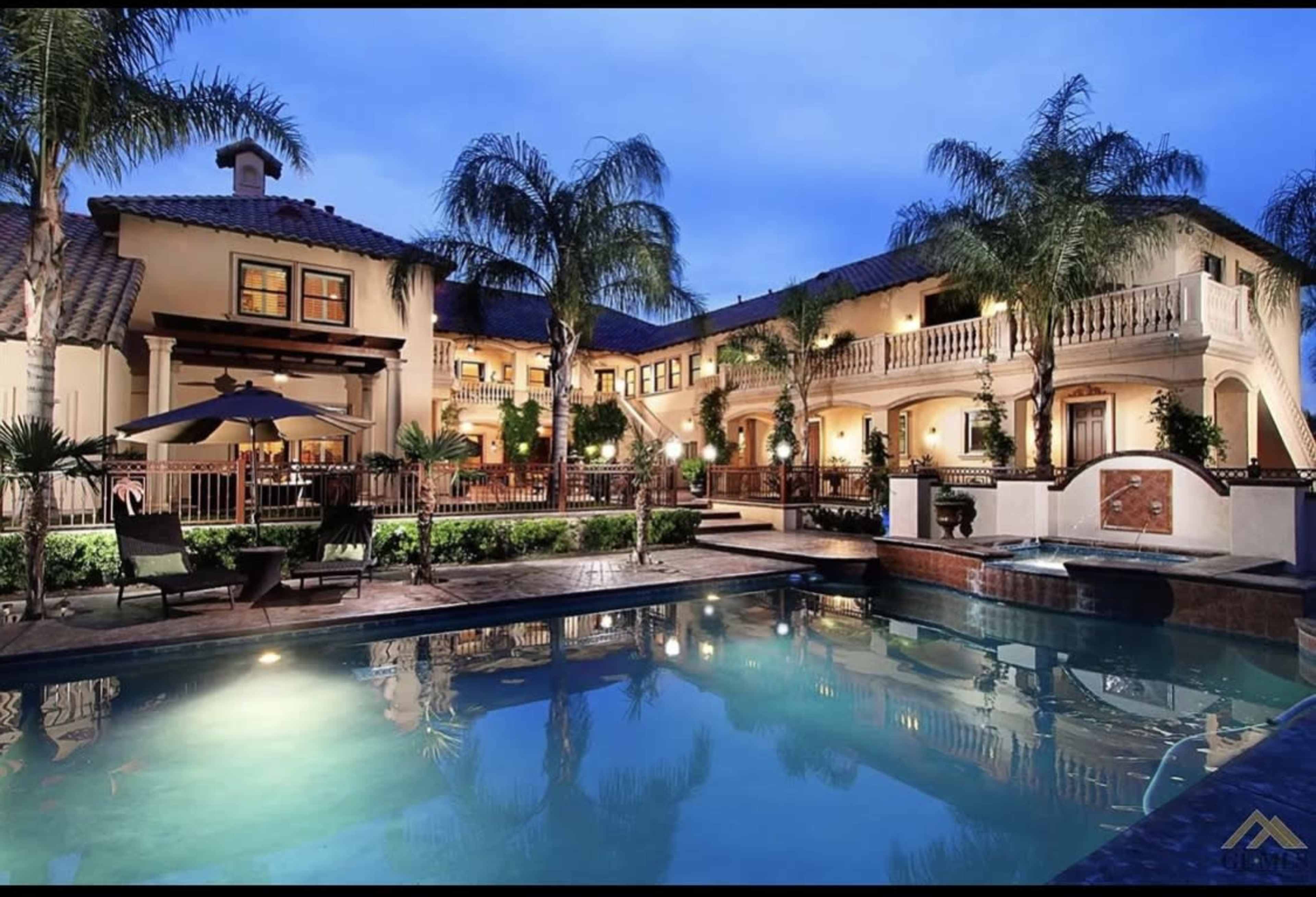 A large, two-story mansion with a pool and palm trees in the foreground.