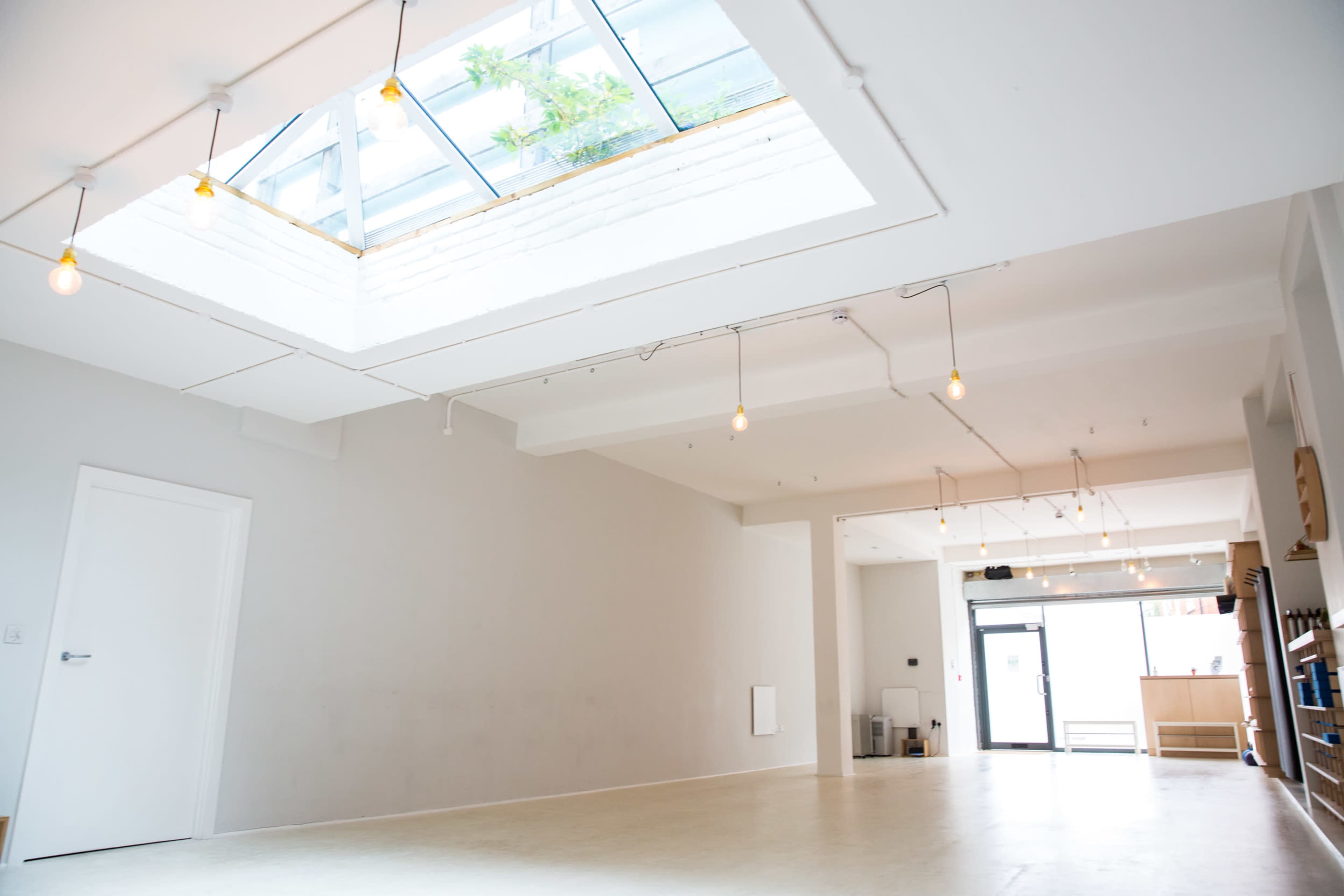 The image shows a bright, modern interior space with wooden flooring, white walls, and a skylight that lets in natural light.