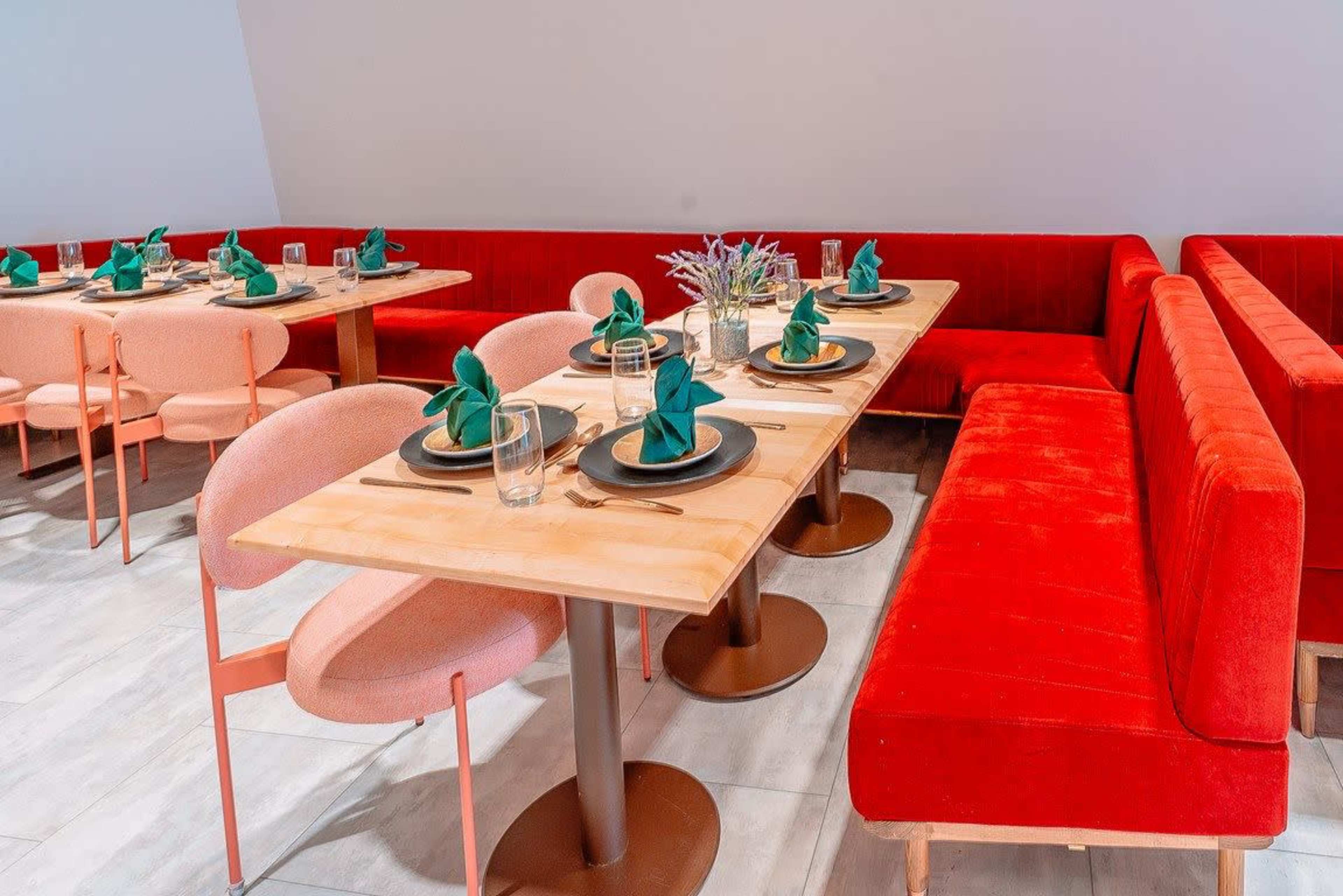 The image shows a restaurant interior with red upholstered seating, wooden tables set with green napkins, and plates arranged for dining.