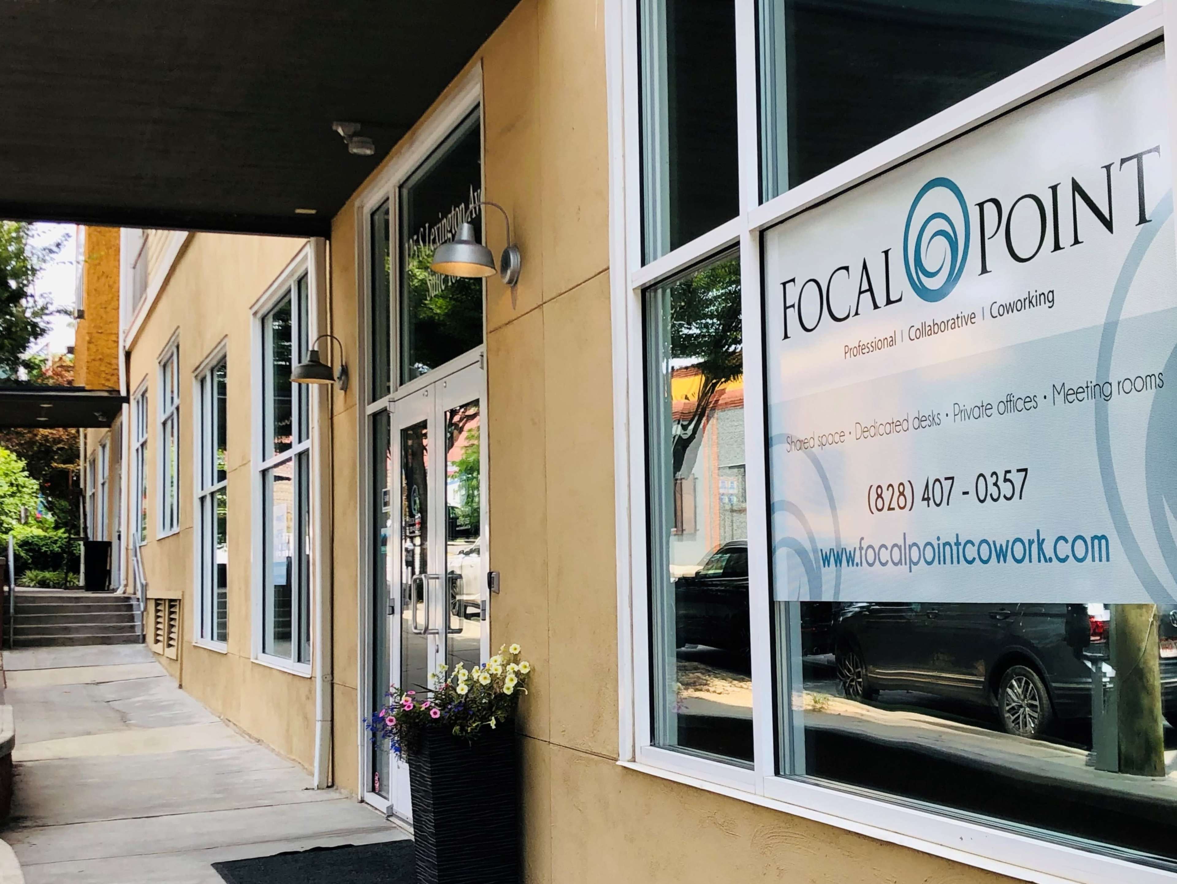 The image shows the entrance of a co-working space called Focal Point, featuring a glass door and a sign displaying its services and contact information.